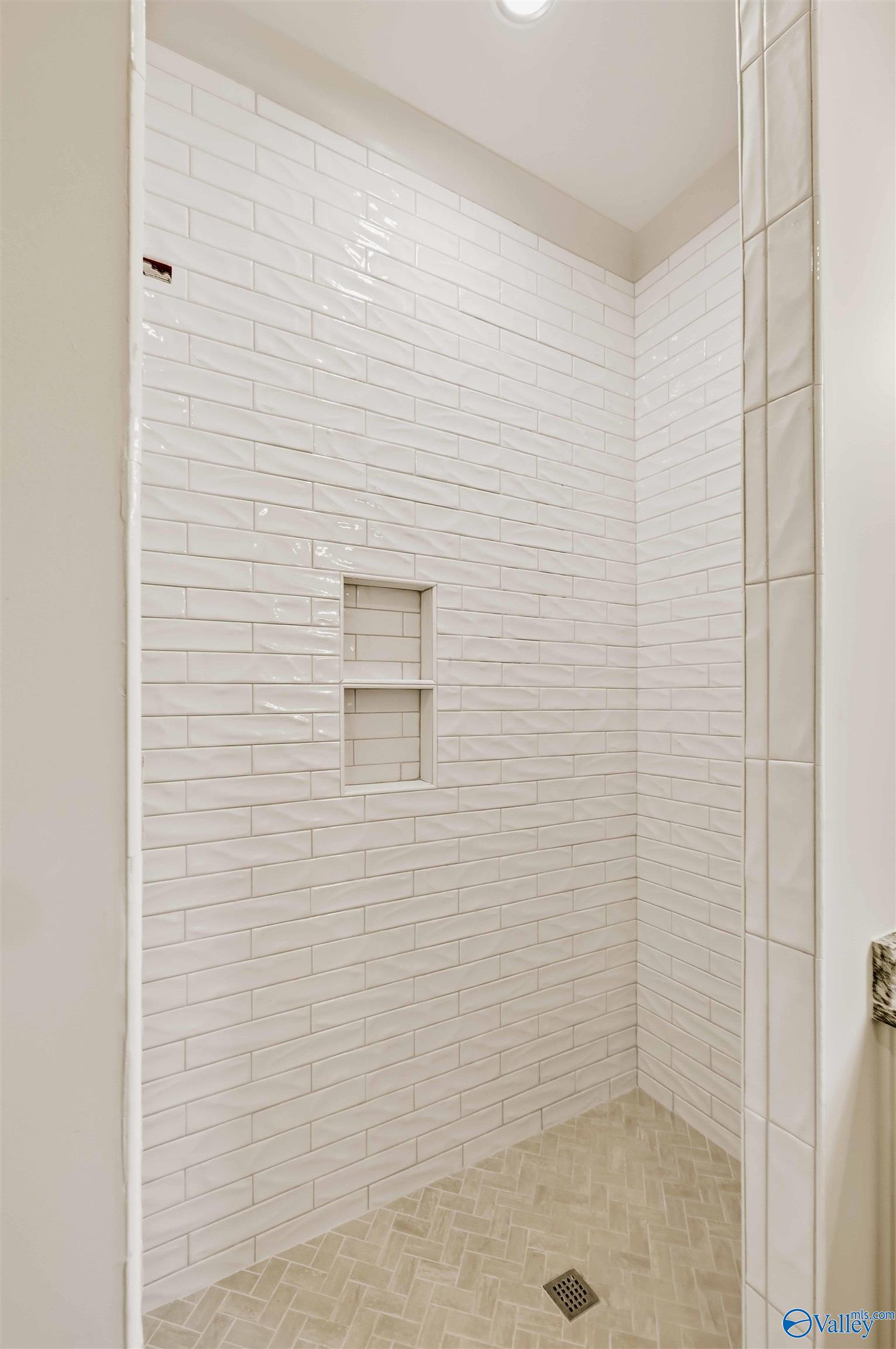 Walk-in shower with glossy white subway tile, two recessed niches, and a beige herringbone tile floor.