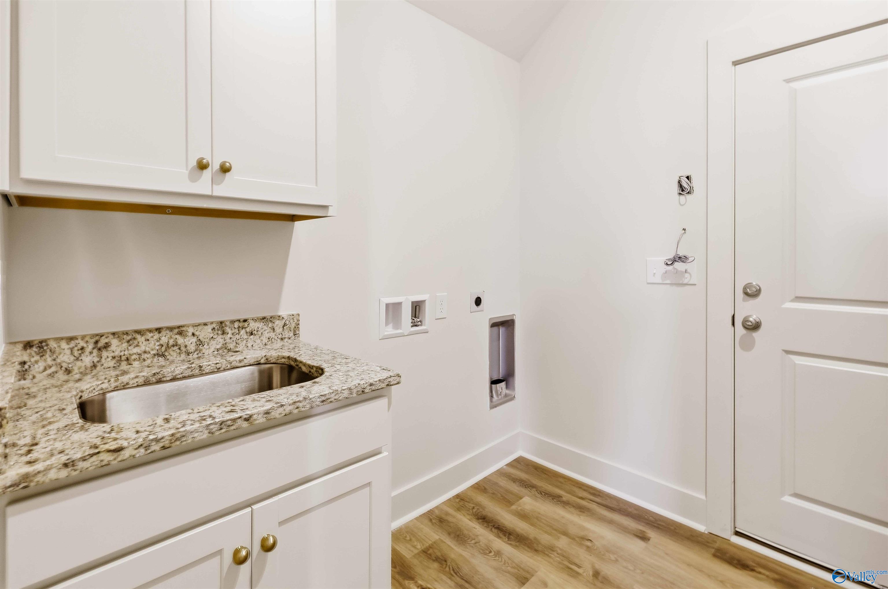 Laundry room with white cabinets, speckled stone counter and utility sink, washer and dryer hookups, and wood-look flooring.