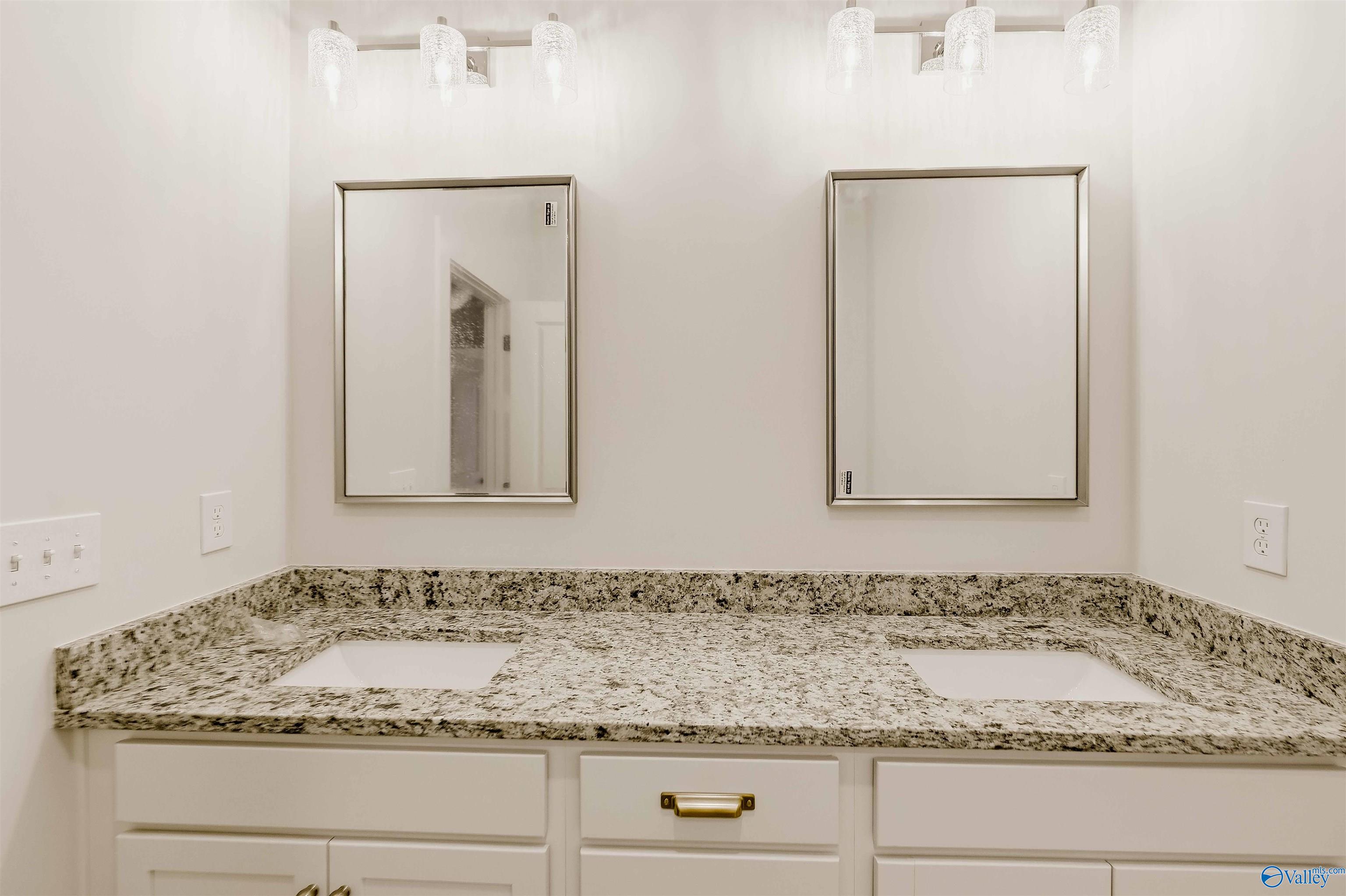 Bathroom vanity with double sinks, speckled granite counters, and two framed mirrors.