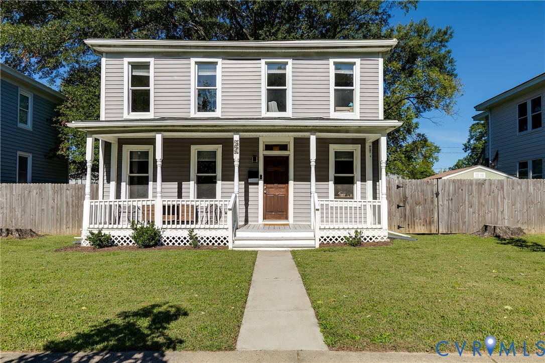 Two-story gray house with a covered porch, white railings, and a walkway across the lawn.