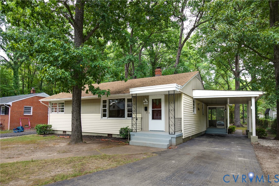 Single-story cream house with a covered entry porch and attached carport beneath mature trees.