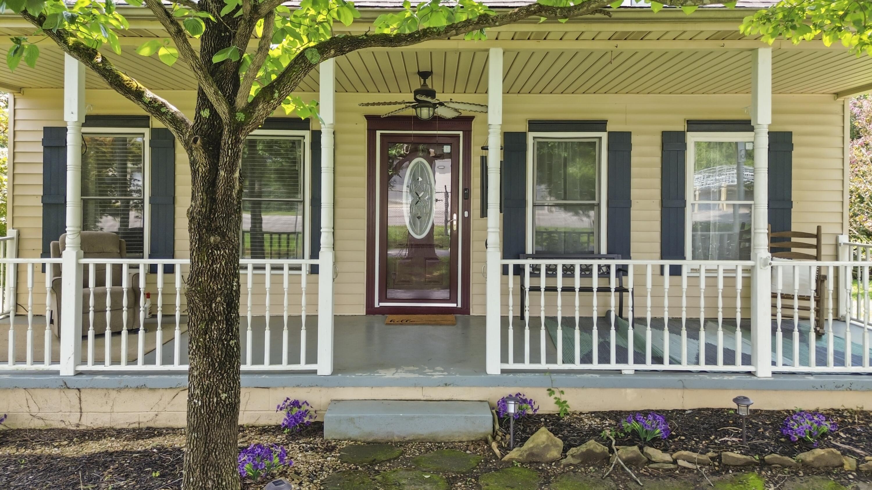 Yellow house with a covered front porch, burgundy glass door, and a large leafy tree in front.