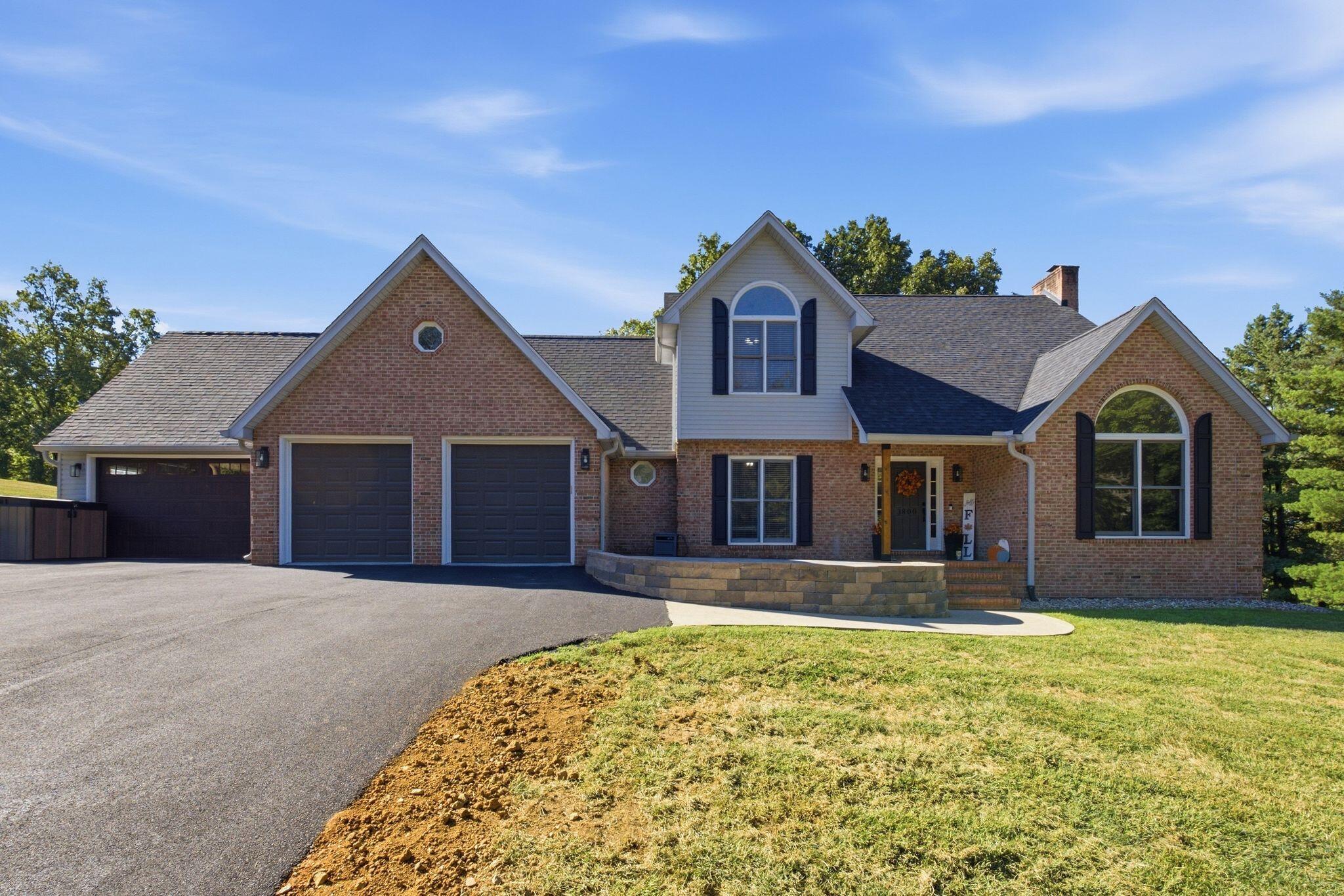 Brick home with three garage doors, arched windows, a curved front porch, and a broad driveway.