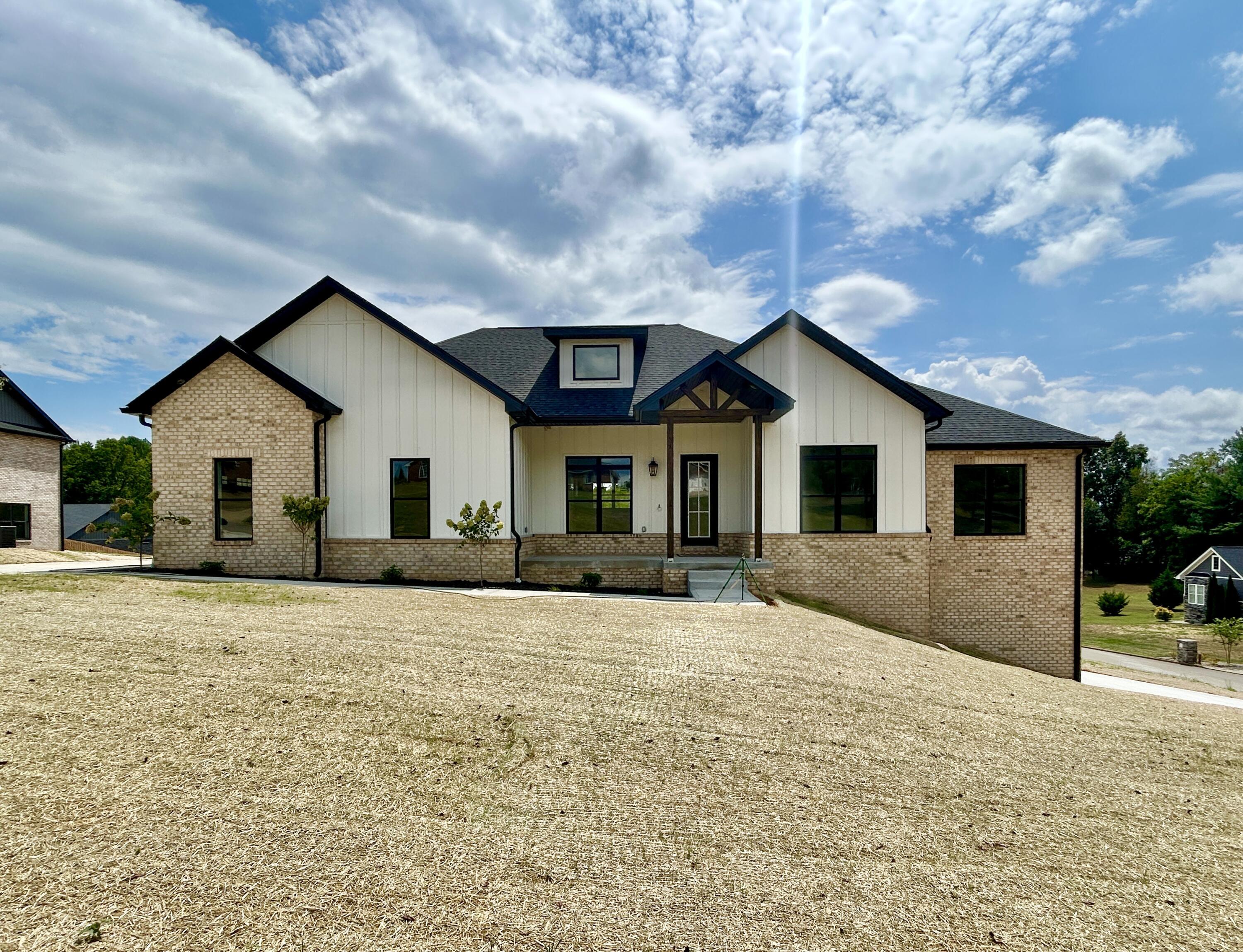 Single-story house with white siding, tan brick accents, and a broad straw-covered front yard.