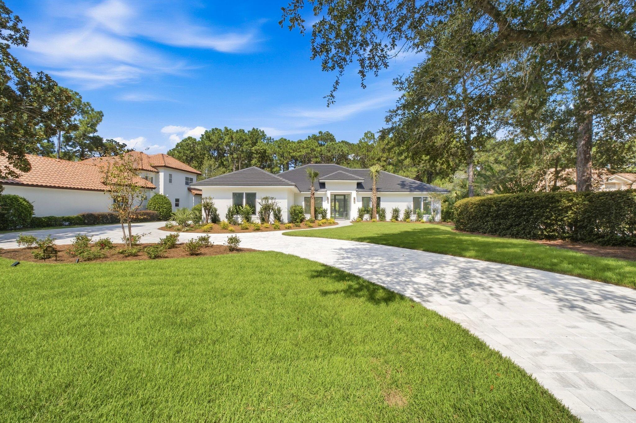 White single-story home with a gray roof, curved stone driveway, and landscaped lawn.