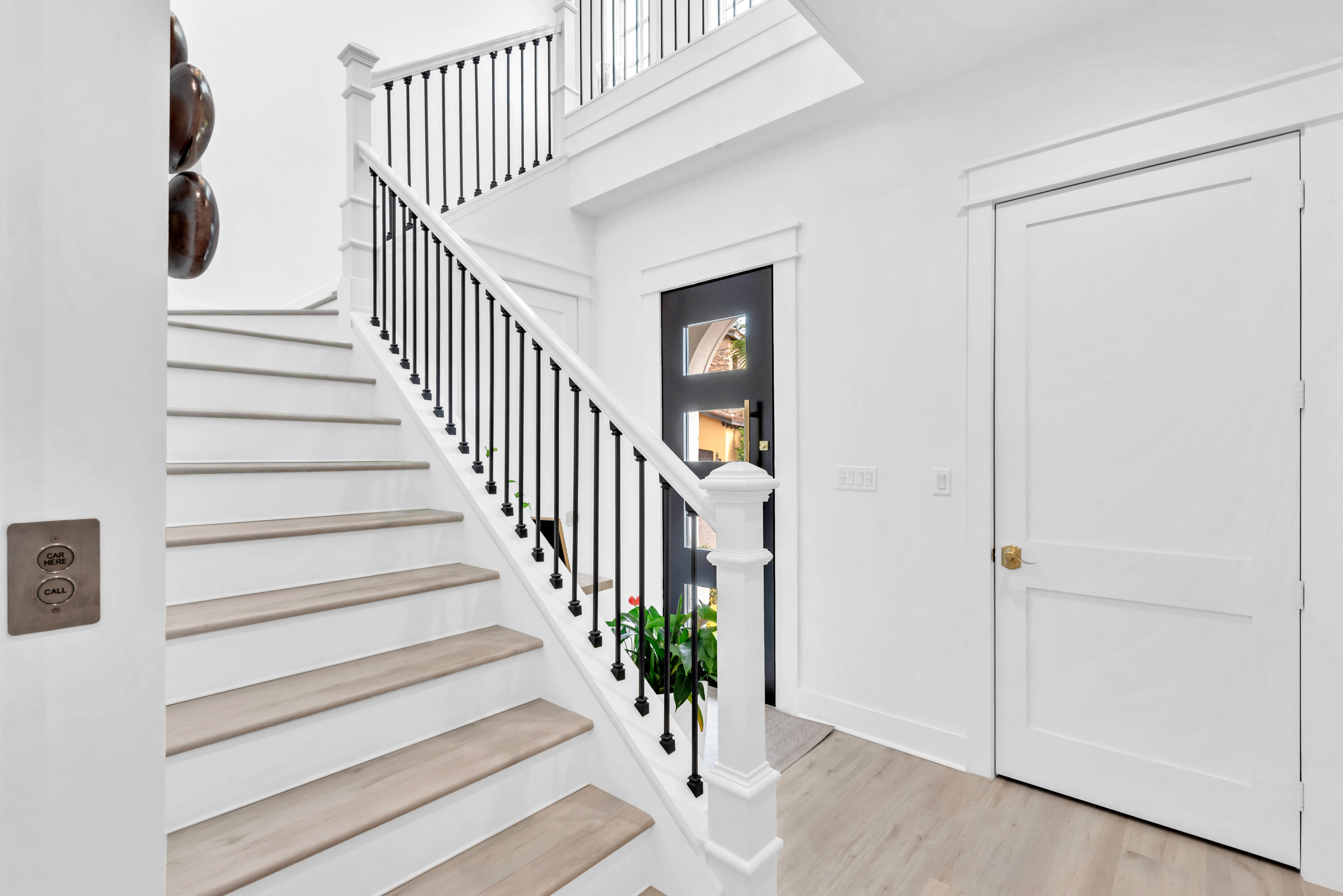 Entry foyer with a light wood staircase, black railings, and a black glass-panel front door.