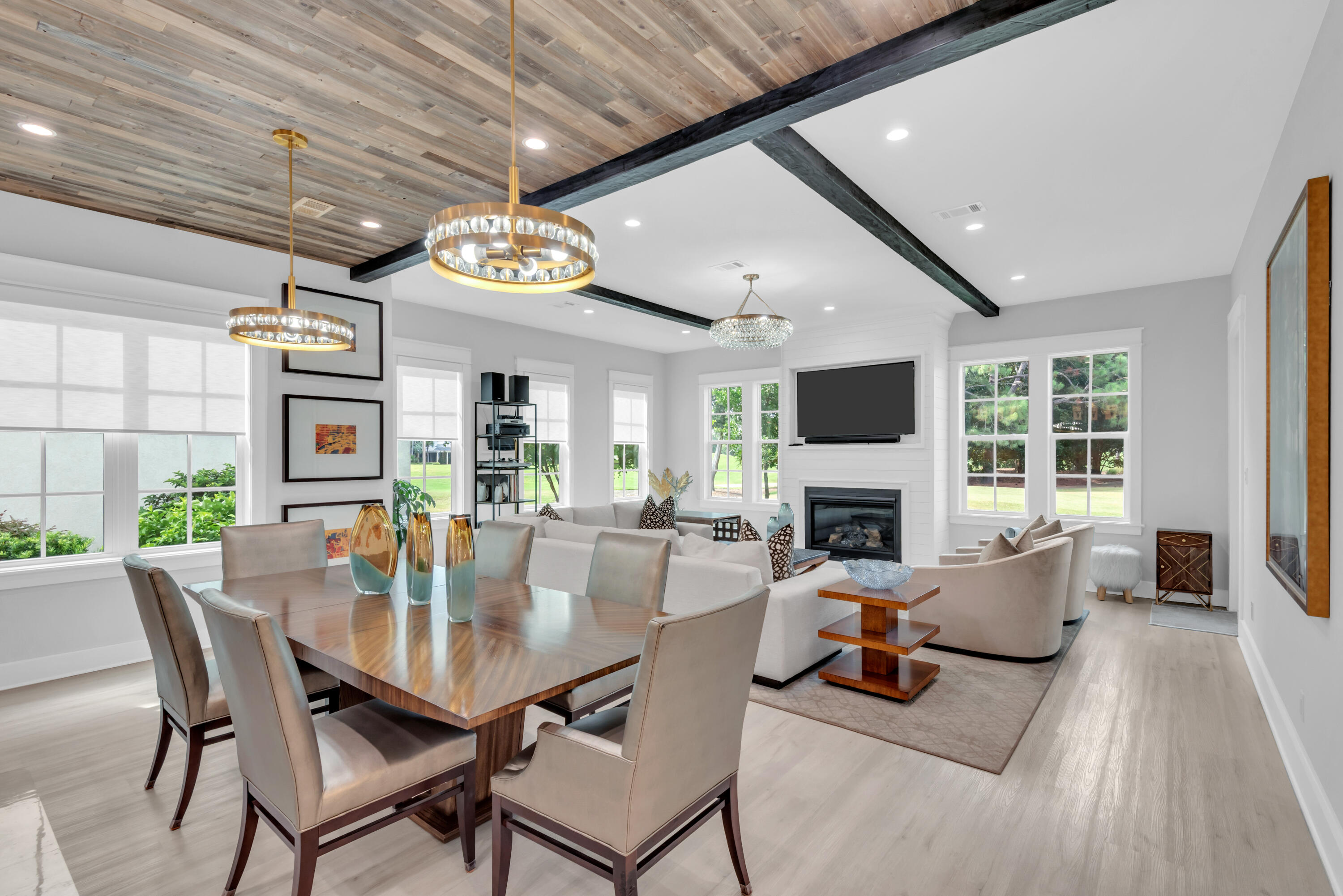 Open living and dining room with a beamed wood ceiling, fireplace, and large windows.