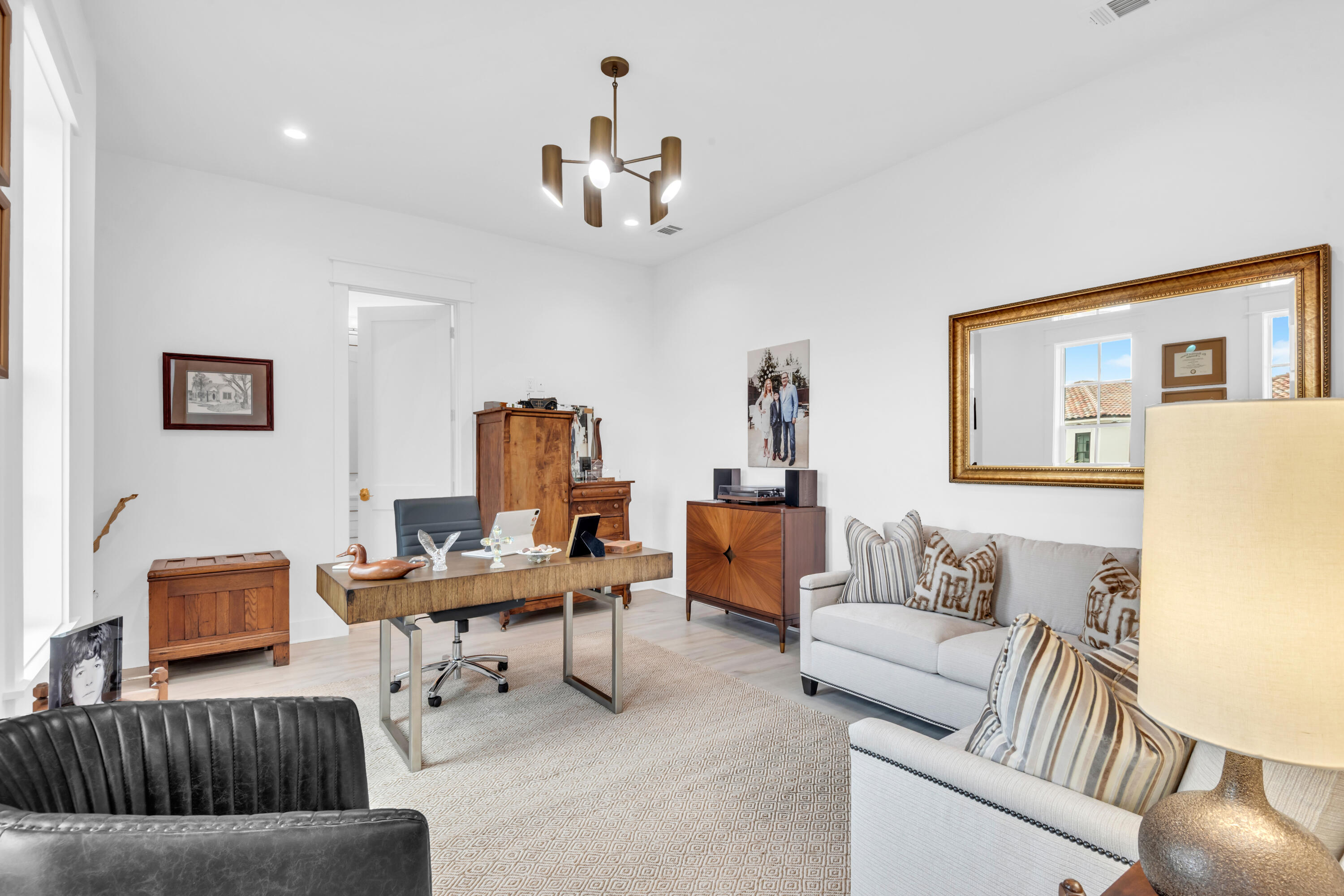 Furnished home office with a large wood desk, white sofas, and a gold-framed mirror.