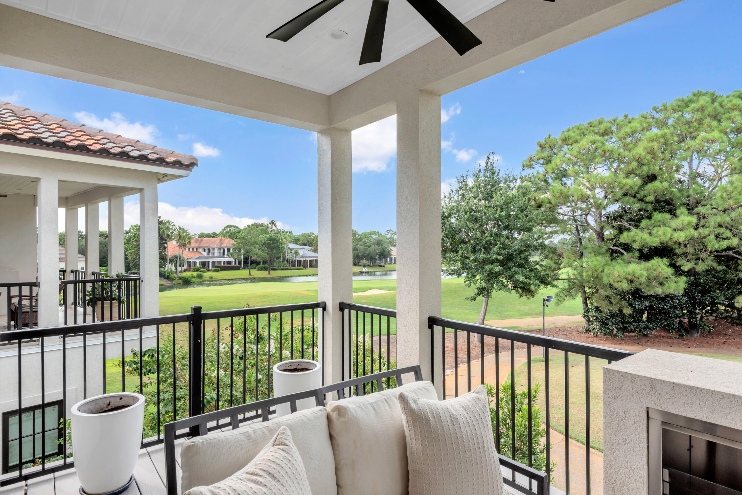 Covered balcony with outdoor sofa and fireplace overlooking a golf course and pond.