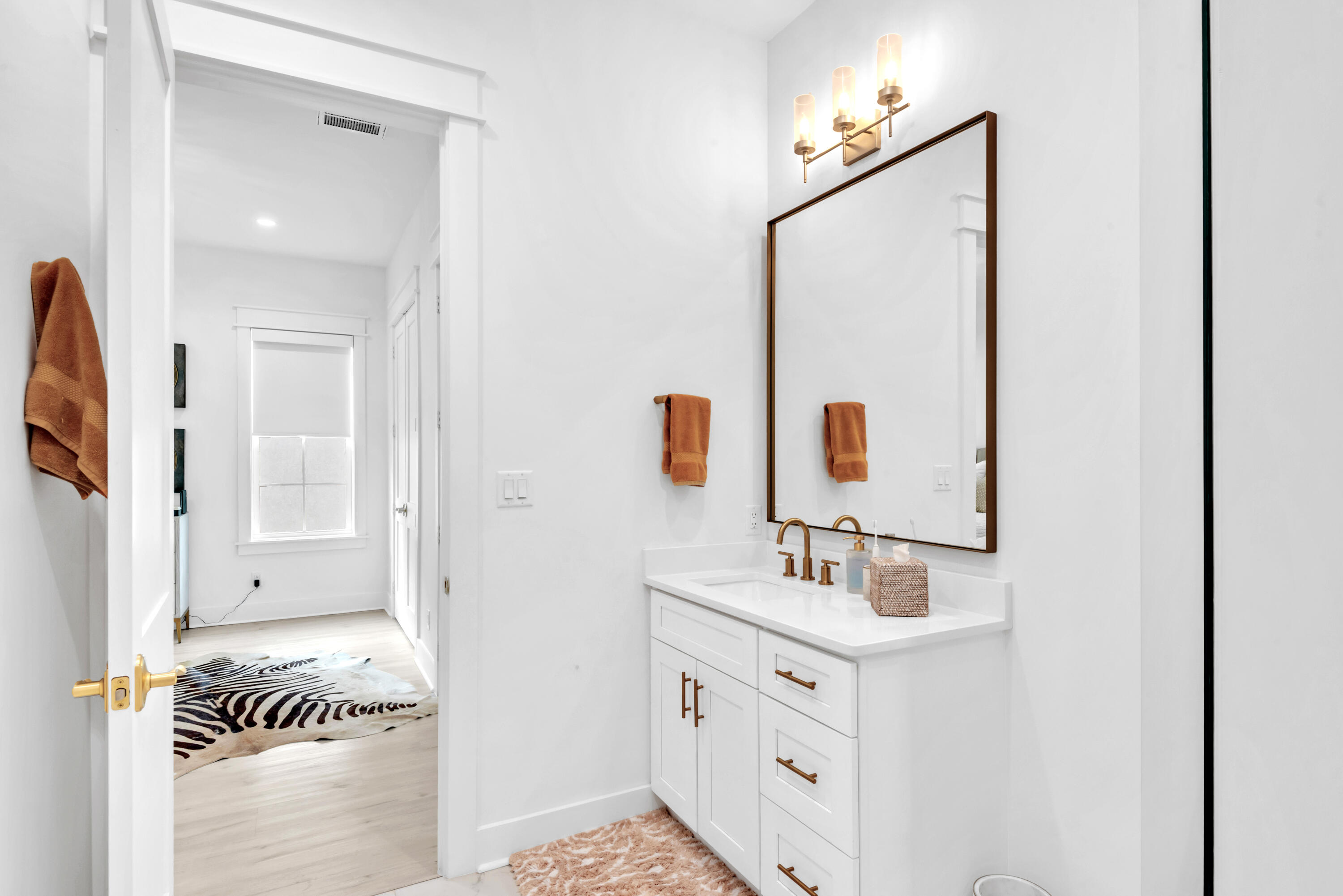 Bright bathroom with a white vanity, brass fixtures, and a large dark-framed mirror.