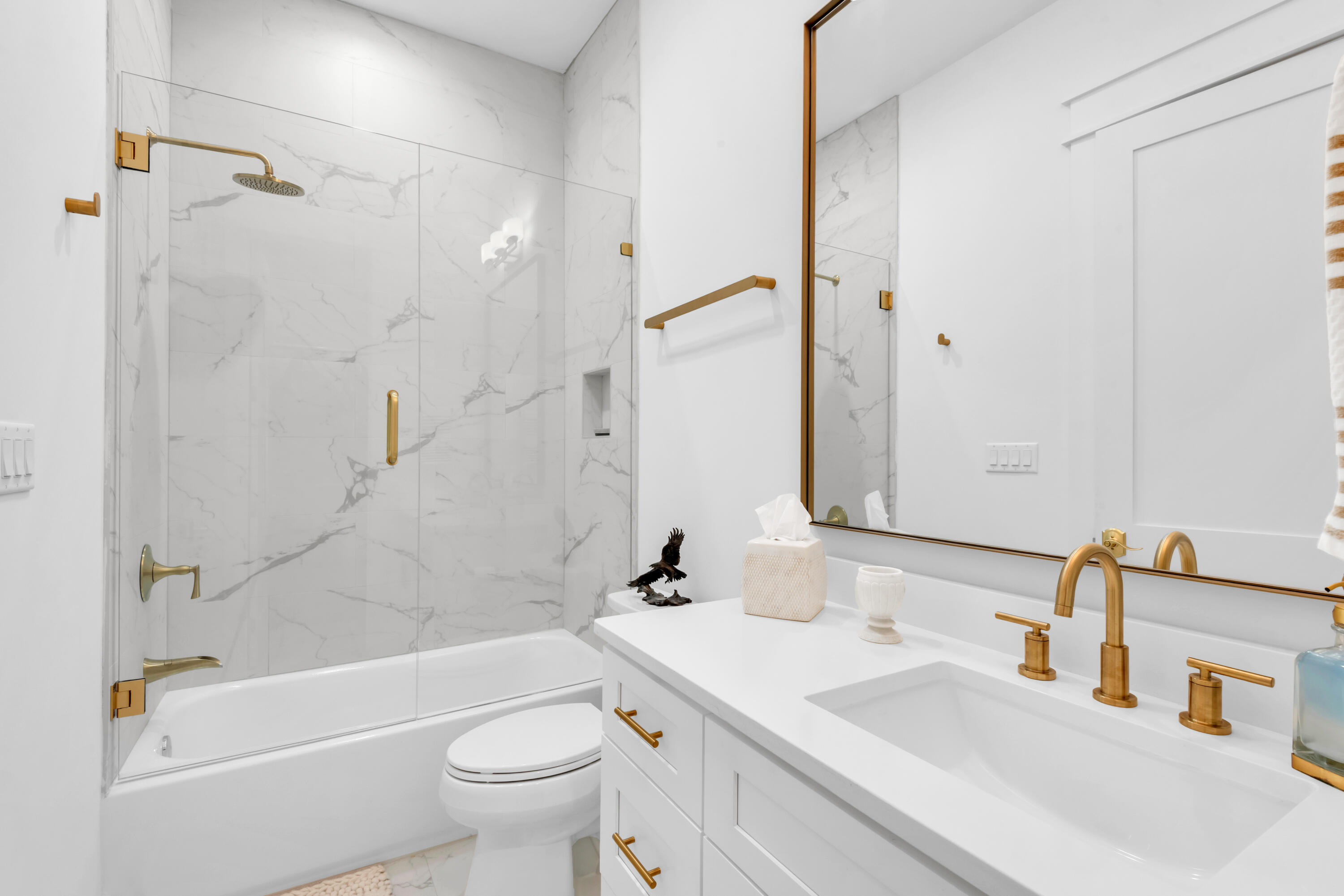 Bathroom with a marble-look tiled tub surround and white vanity with gold fixtures.