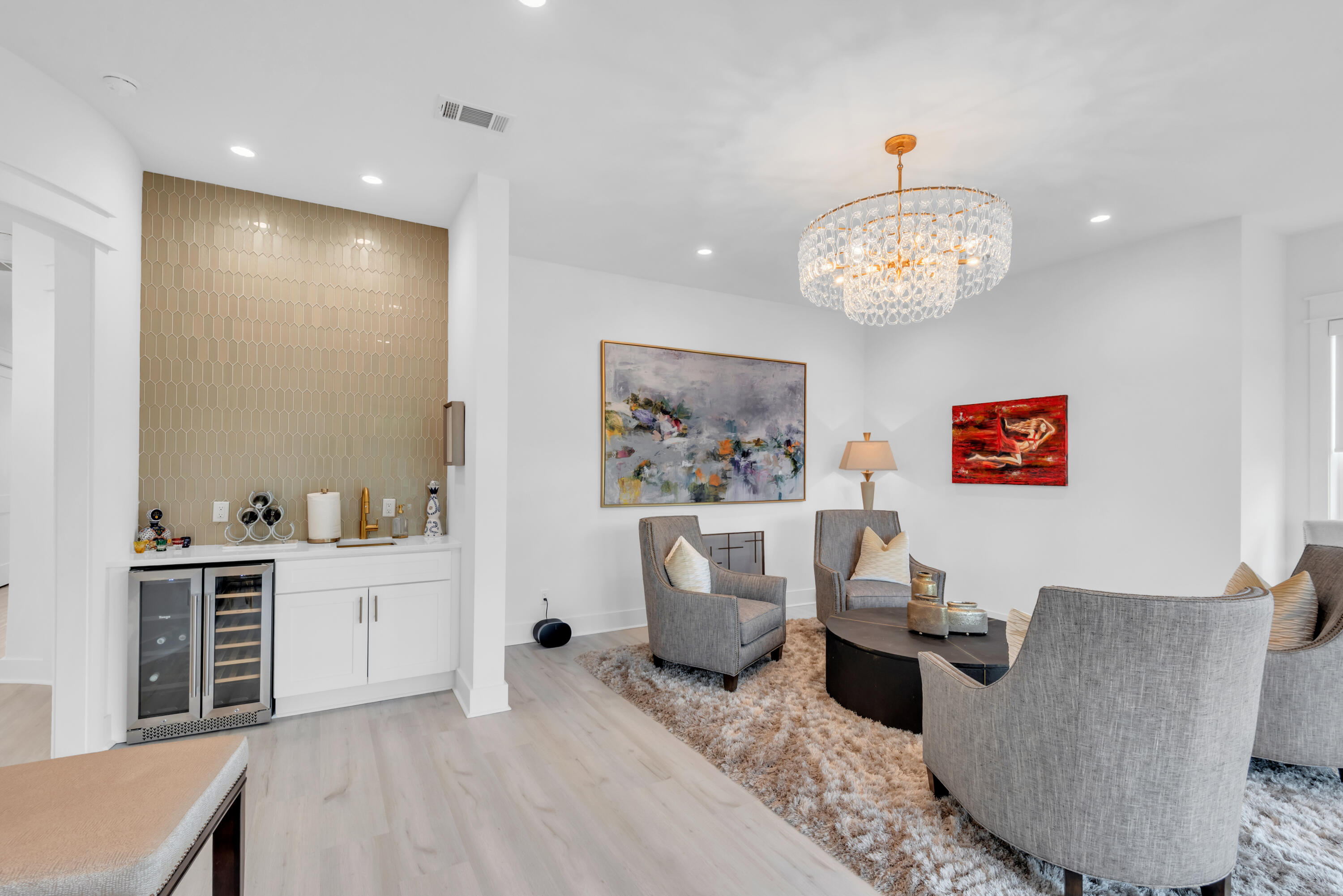 Living room with gray armchairs, a crystal chandelier, and a wet bar with gold tile backsplash.