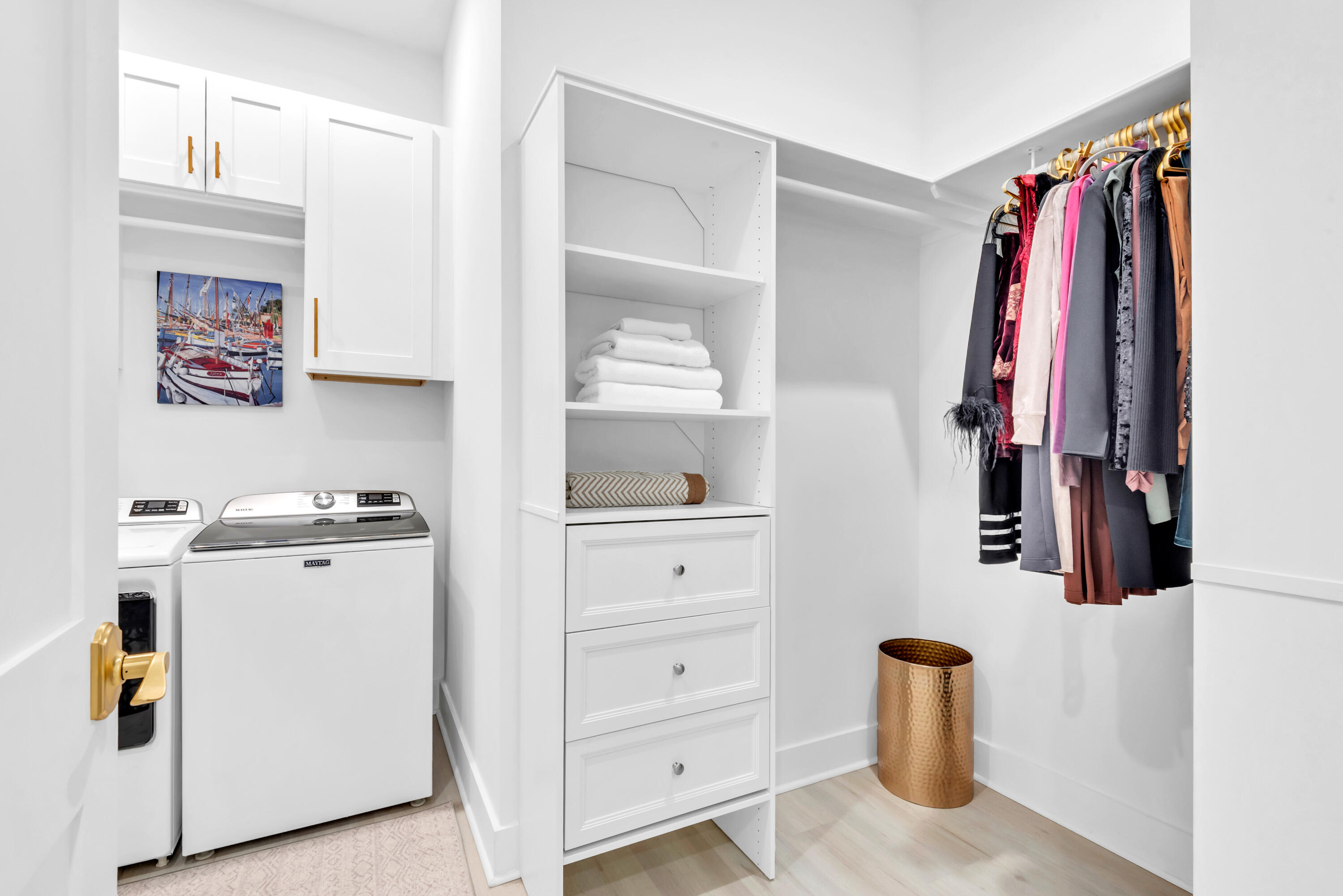 Laundry room with washer and dryer beside built-in linen shelves and hanging clothes.