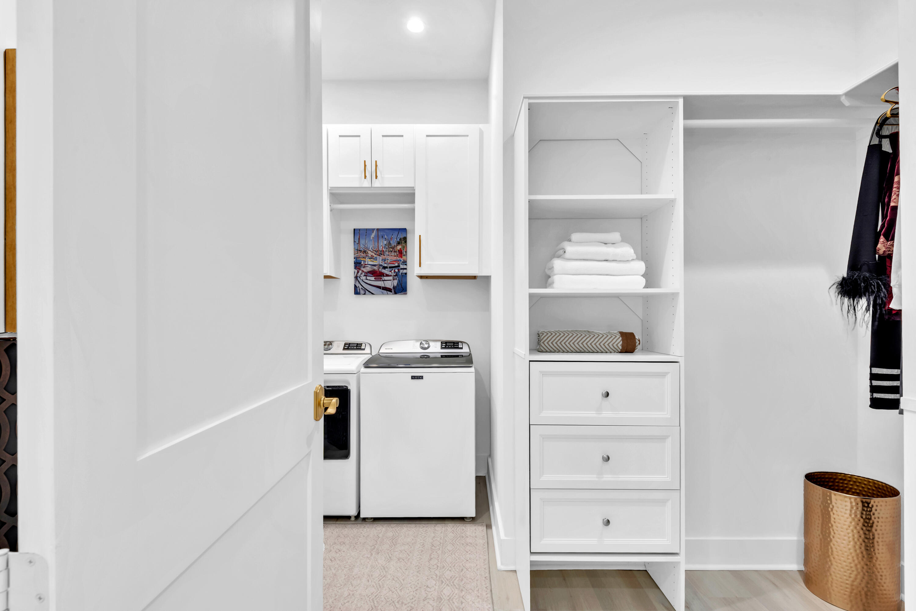 Laundry room with washer and dryer beside built-in shelving, drawers, and hanging clothes.