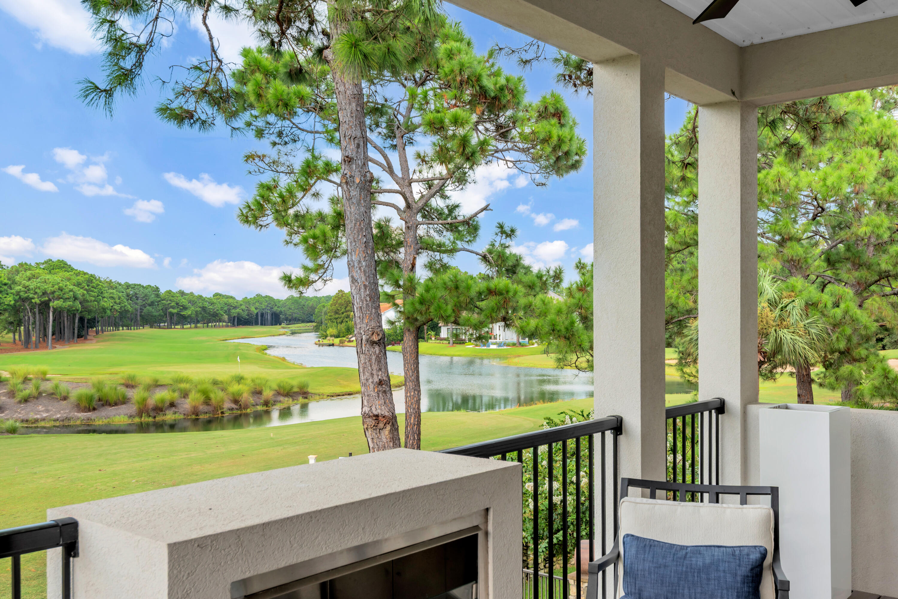 Covered balcony overlooking a golf course and pond, with pine trees and an outdoor fireplace.