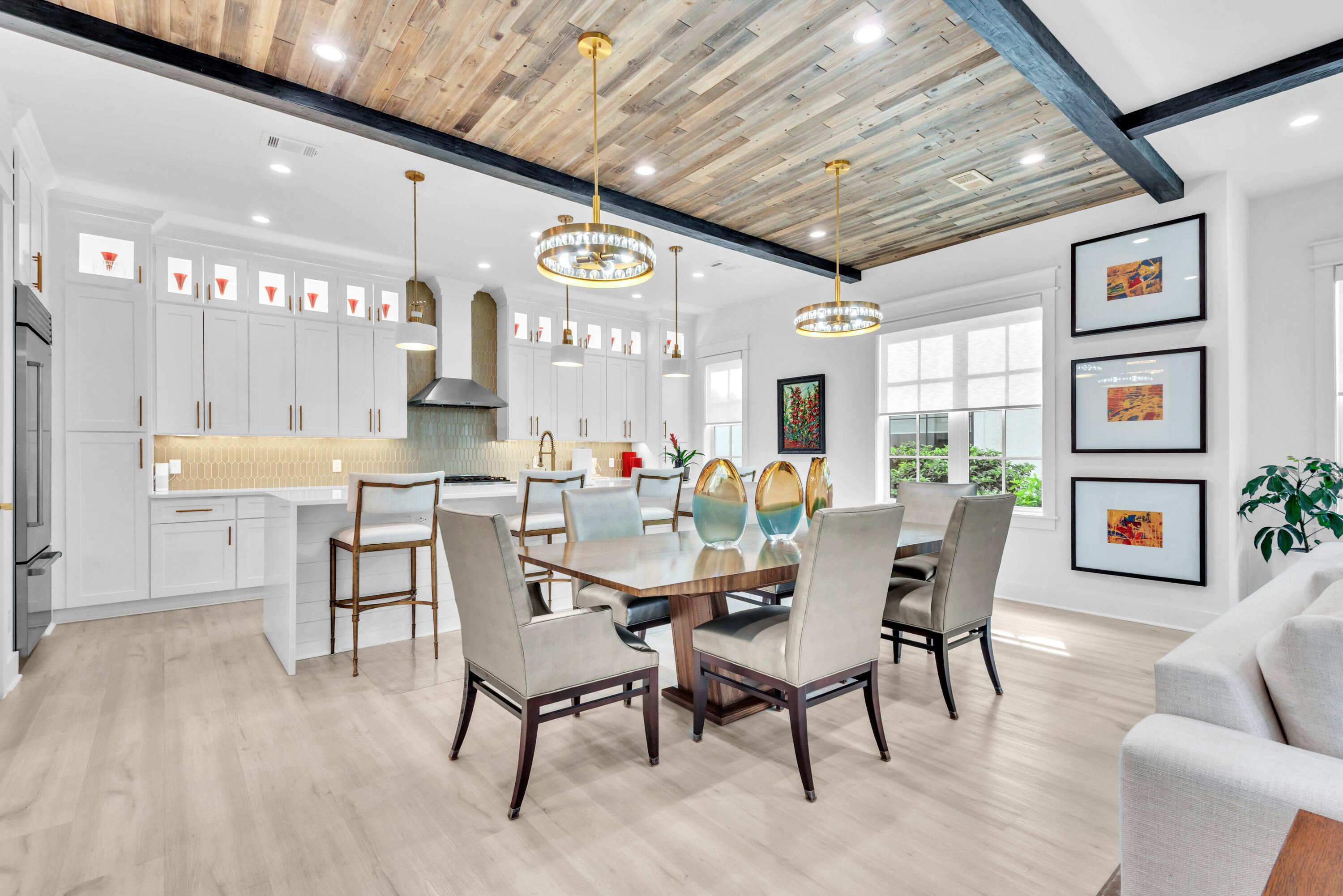 Open-plan kitchen and dining area with white cabinets, a wood-plank ceiling, and a furnished dining table.