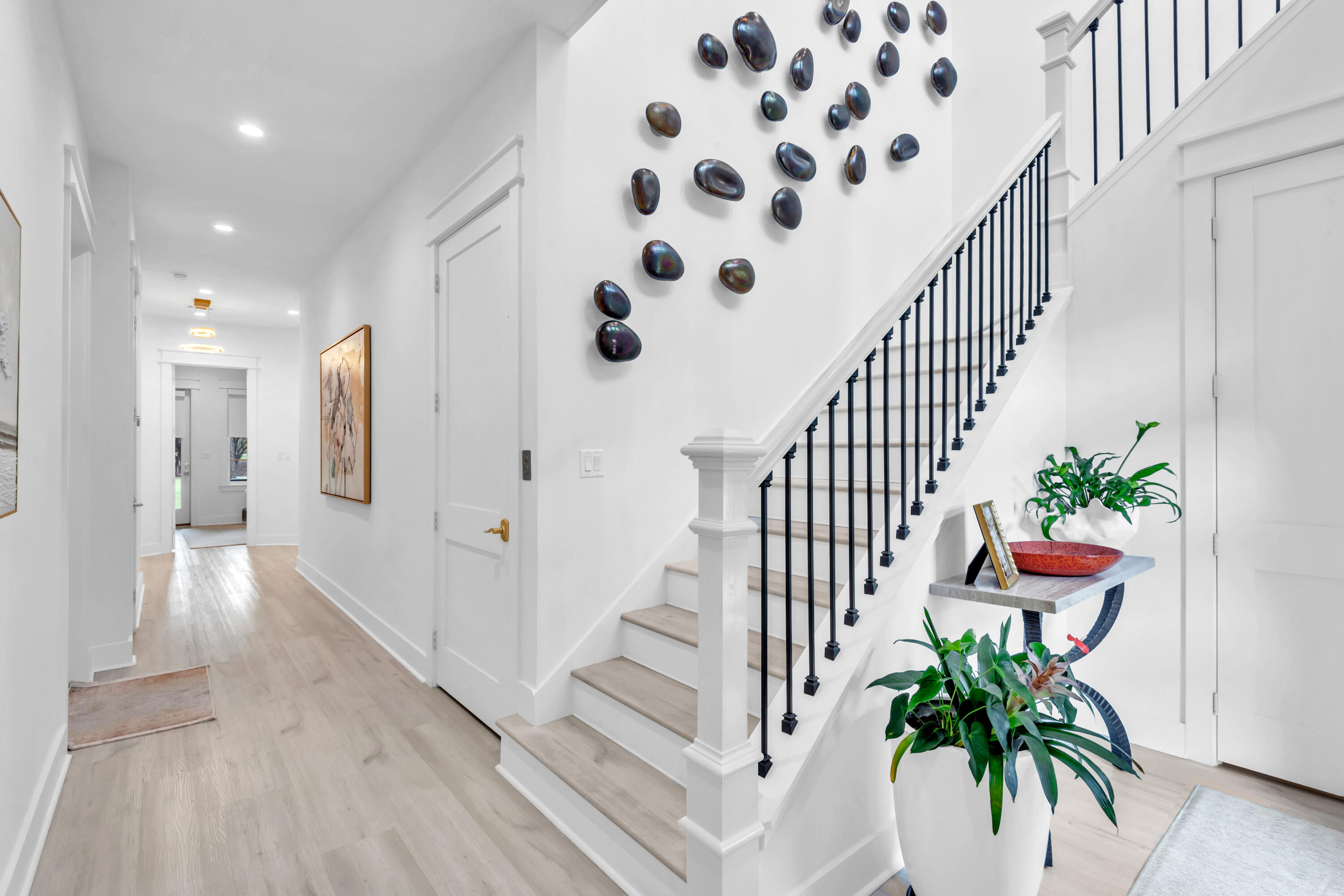 Bright entry foyer with a light wood floor, dark-railed staircase, and sculptural wall decor.