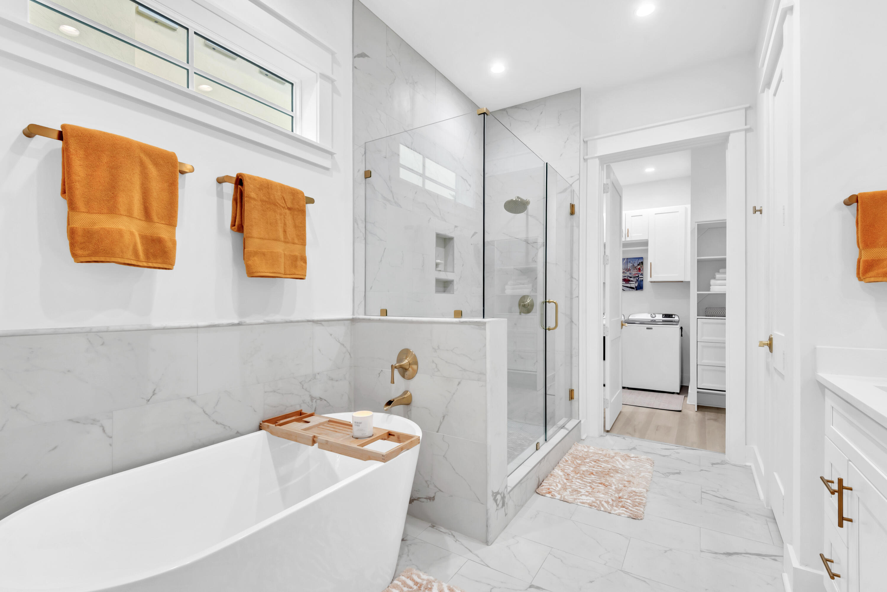 Staged bathroom with a freestanding tub, marble shower, gold fixtures, and orange towels.