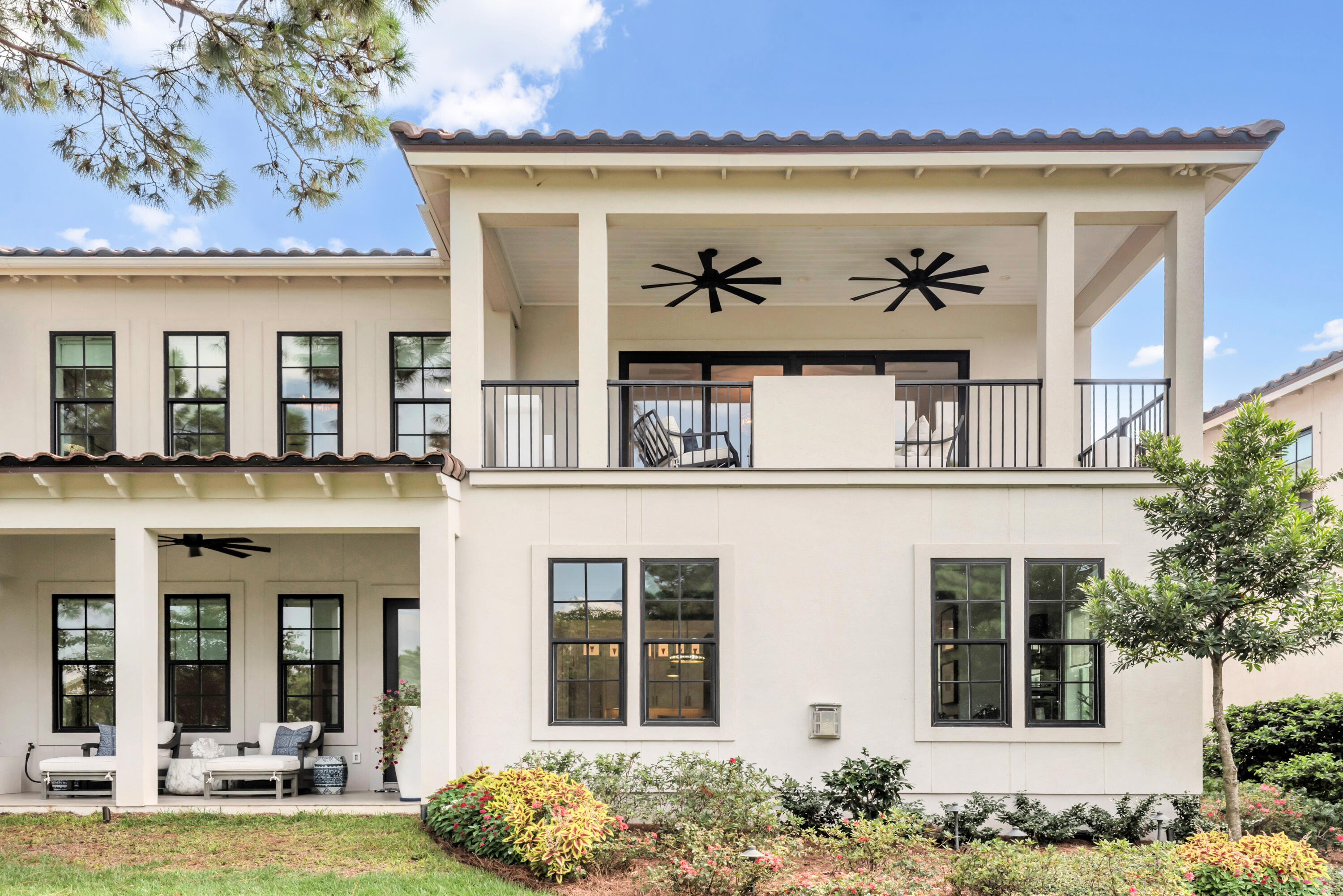 Two-story cream home with a covered balcony, twin ceiling fans, and a furnished patio.