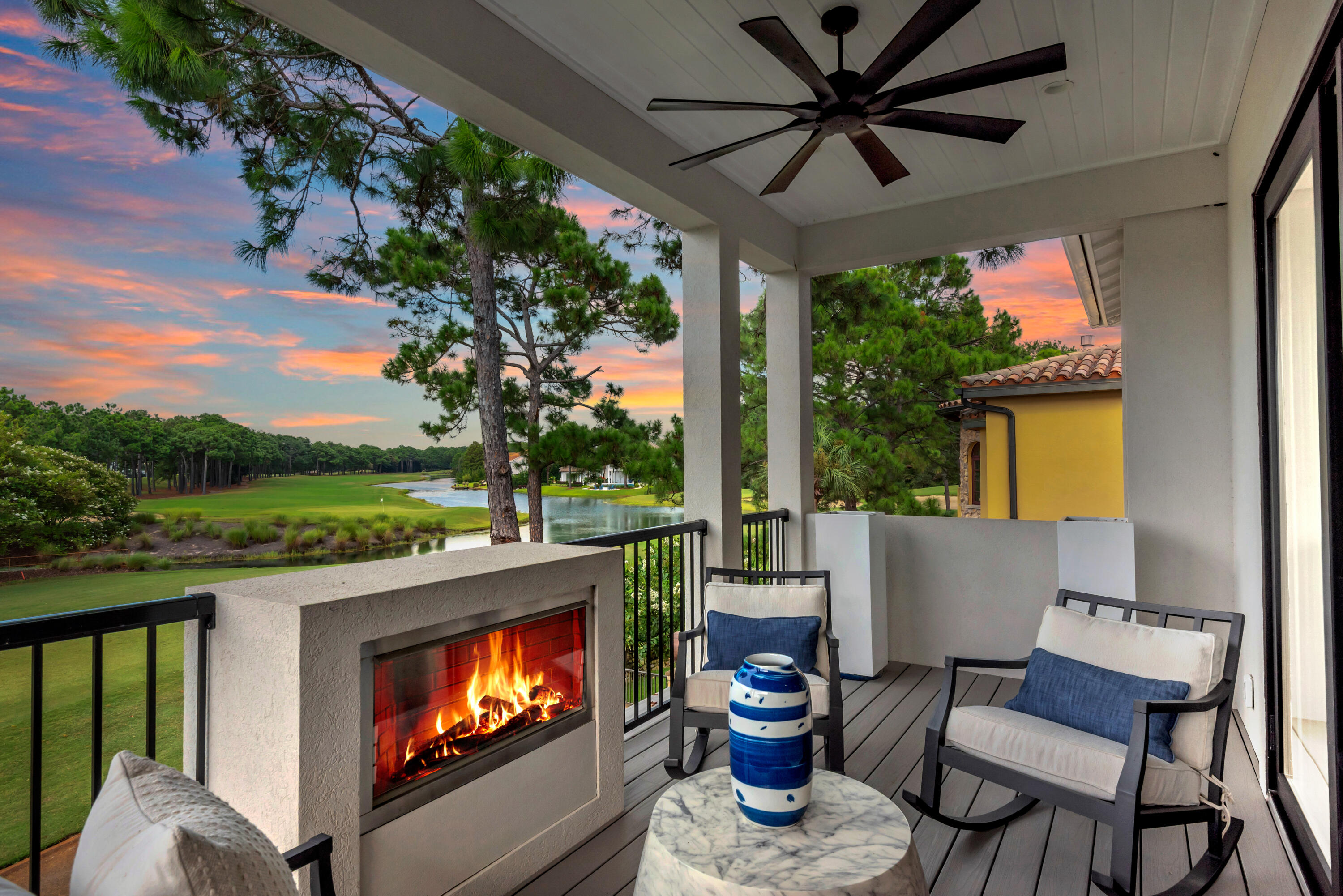 Covered balcony with fireplace and rocking chairs overlooking a golf course and pond at sunset.