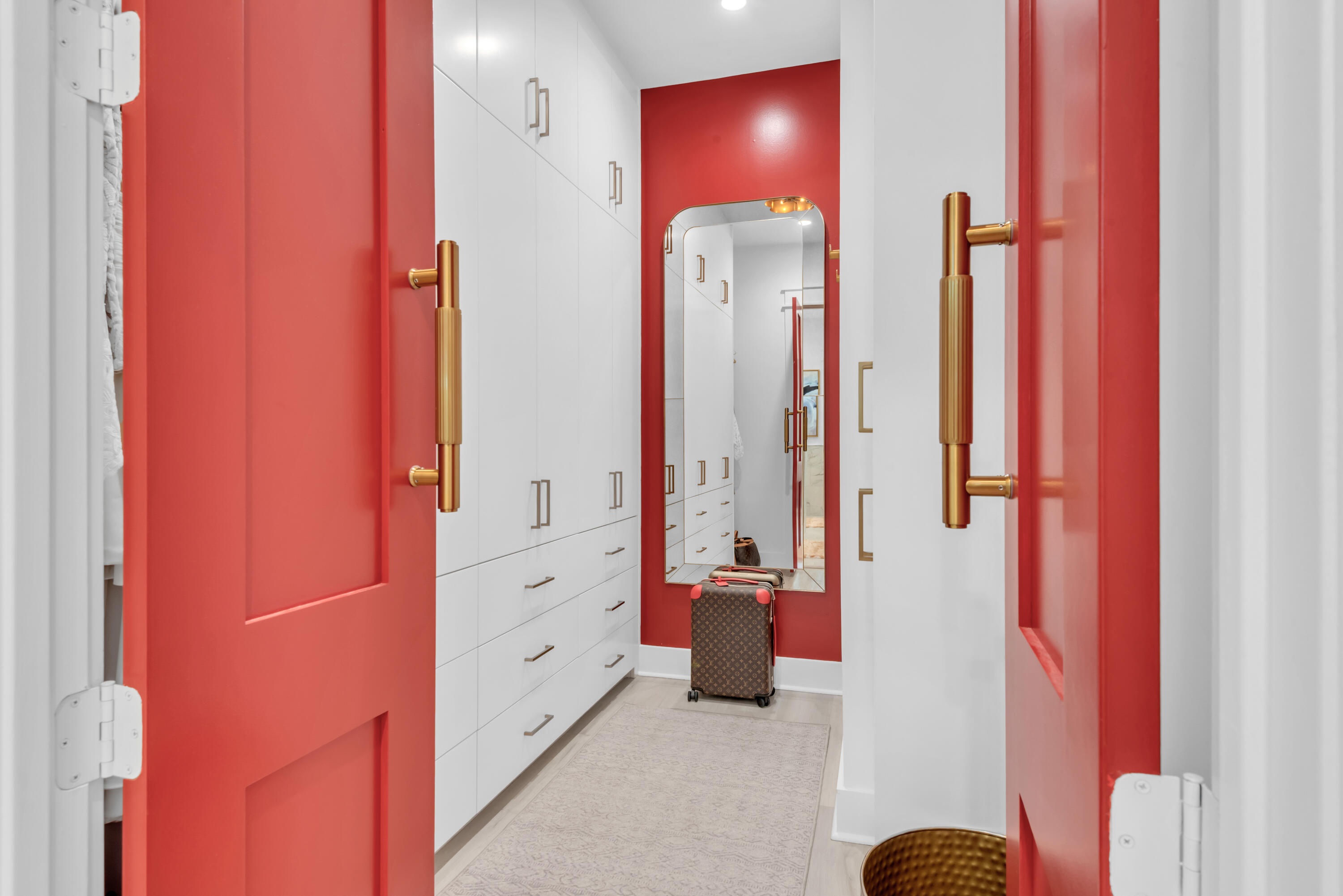 Walk-in dressing room with white built-in wardrobes, red walls, brass hardware, and a full-length mirror.