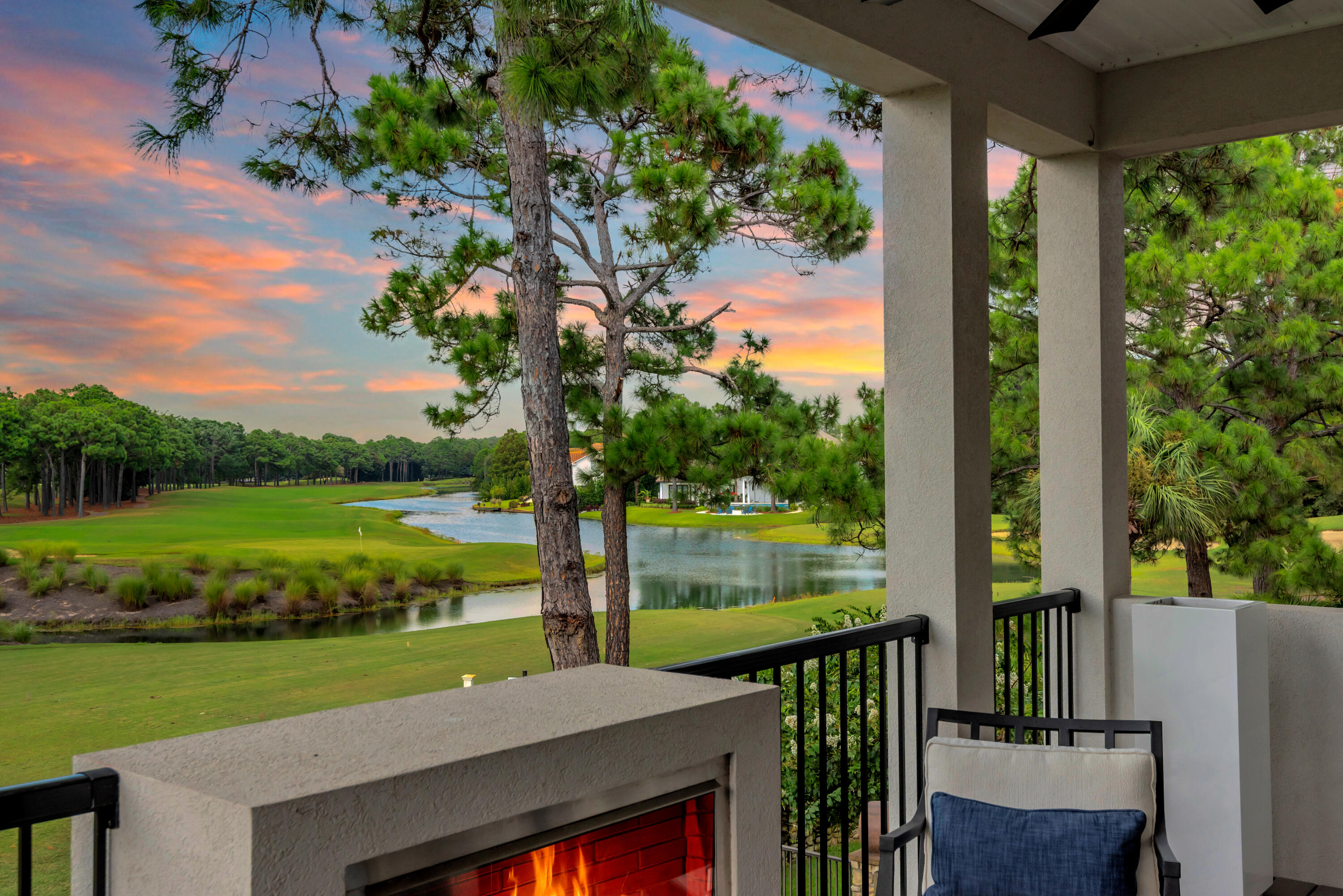 Covered balcony with a fireplace overlooking a golf course and pond at sunset.