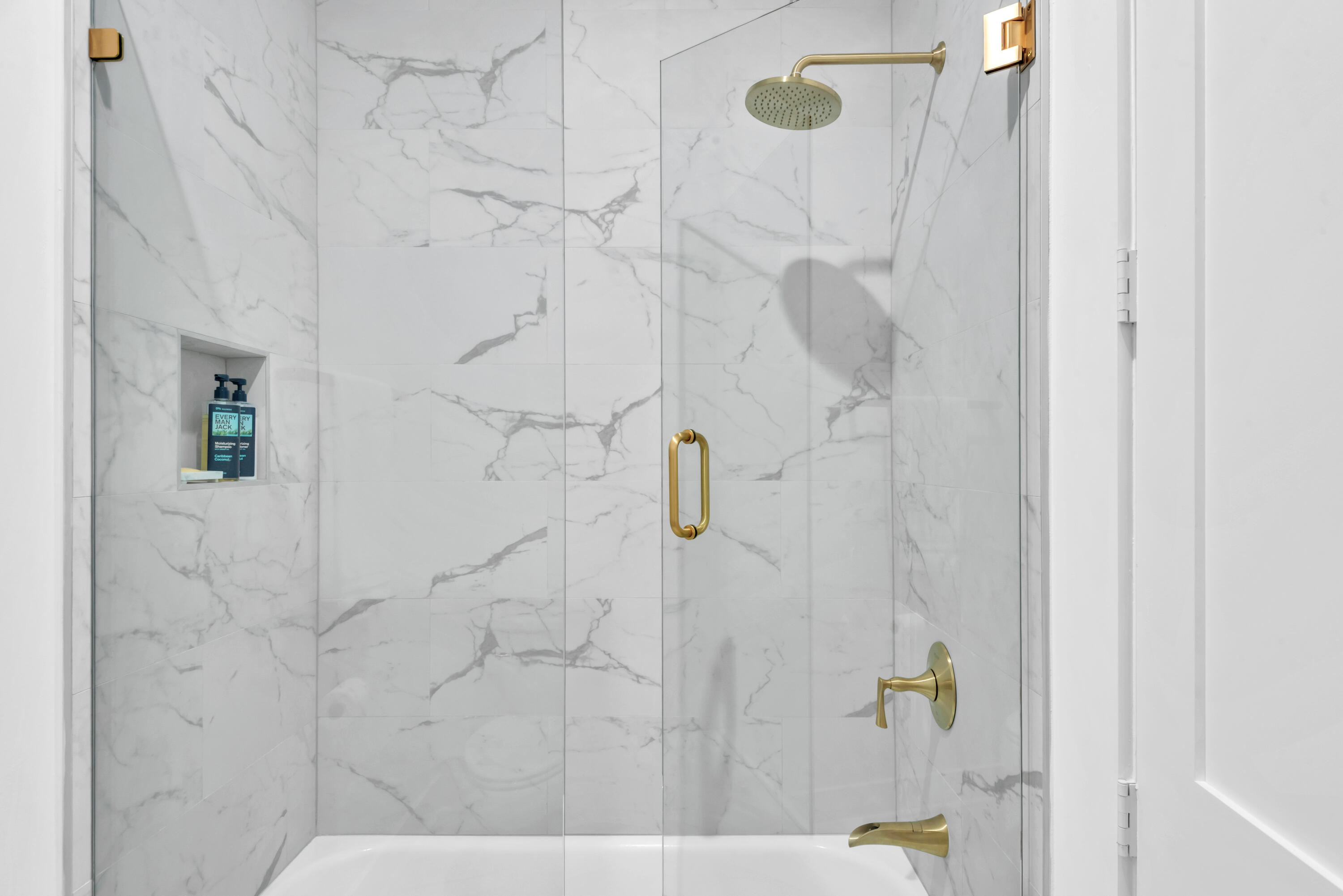 Marble-look walk-in shower with brass fixtures, glass enclosure, and recessed toiletry niche.