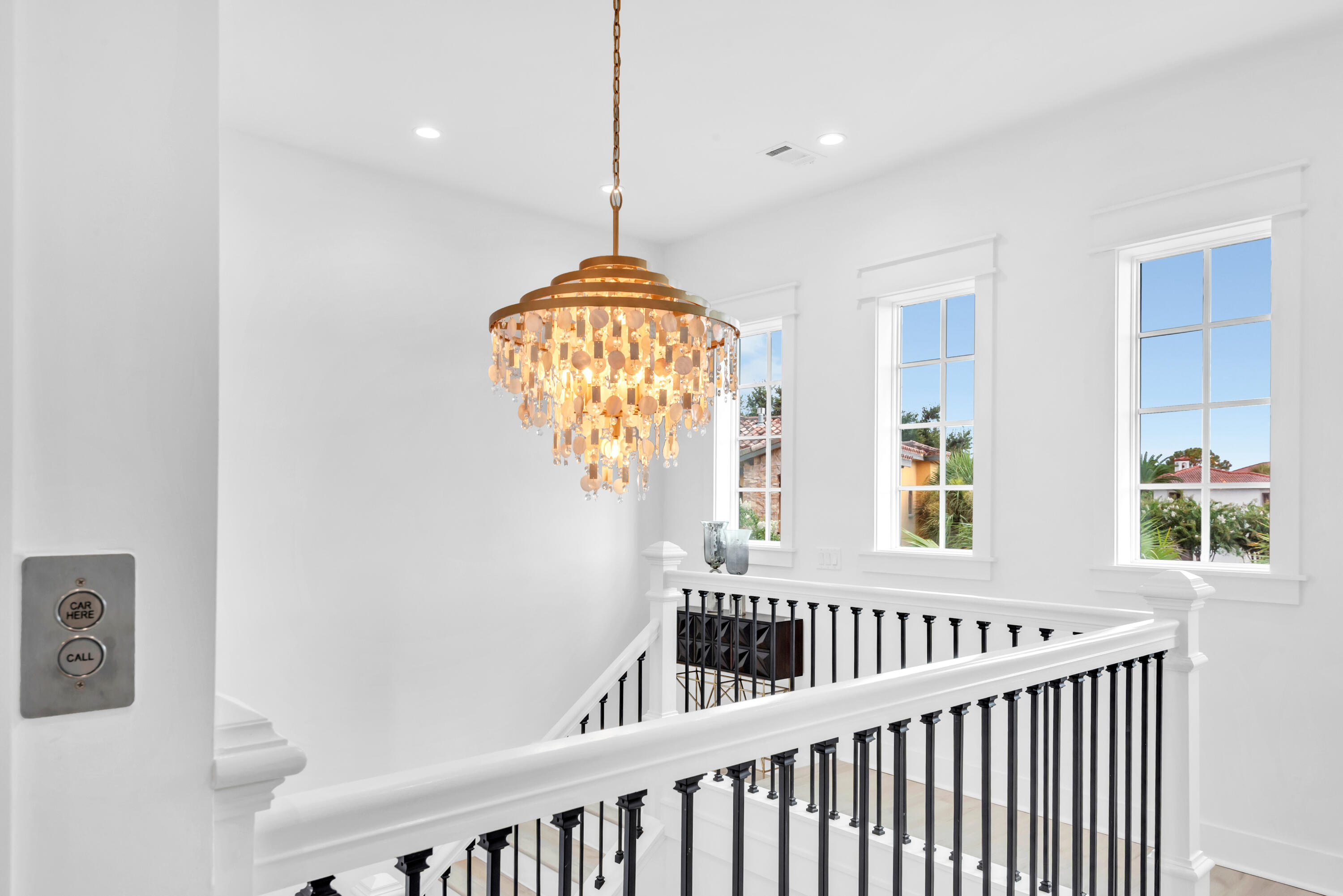 Stair landing with a crystal chandelier, black balusters, and tall windows.