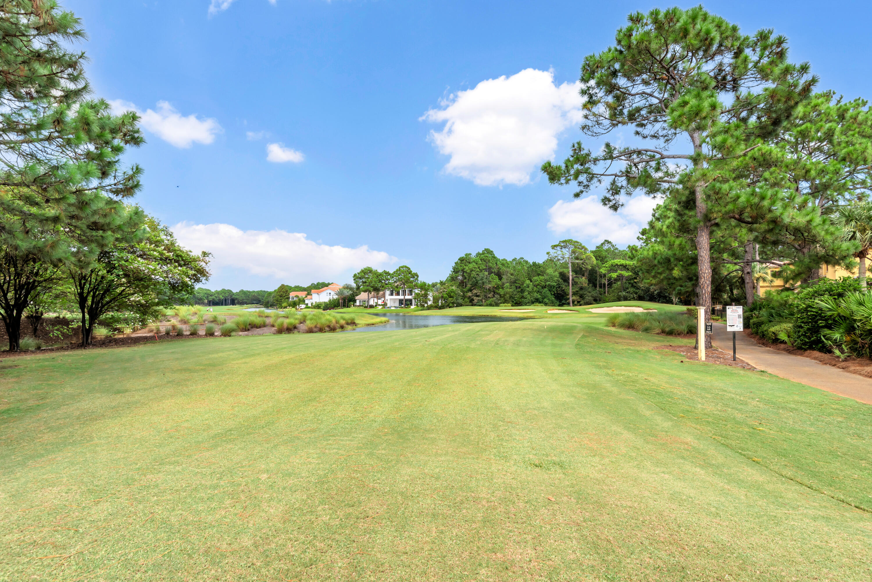 Golf course with a pond and sand bunkers, framed by pine trees and distant homes.