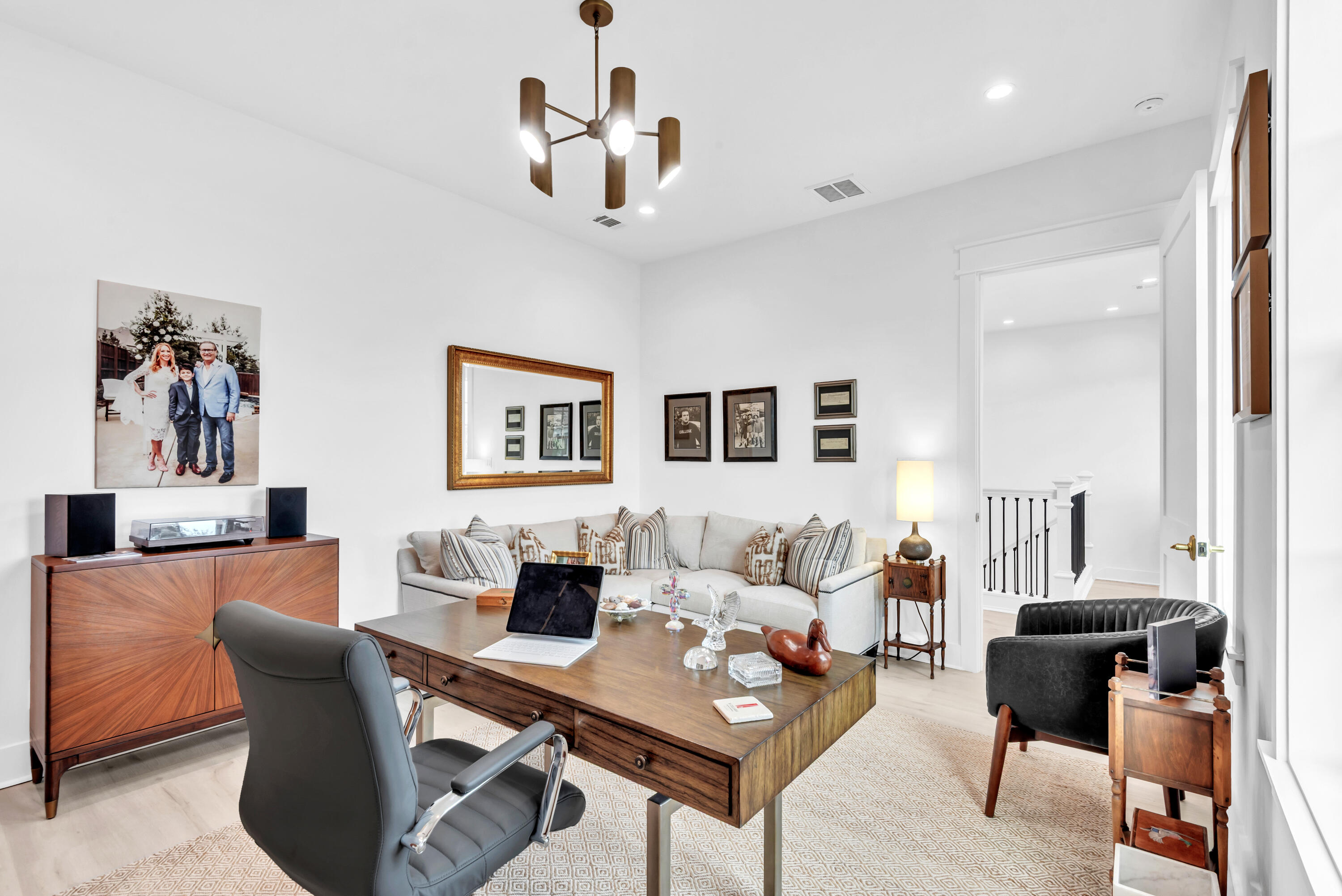 Home office with a wooden desk, gray chair, cream sectional, and doorway to the staircase.