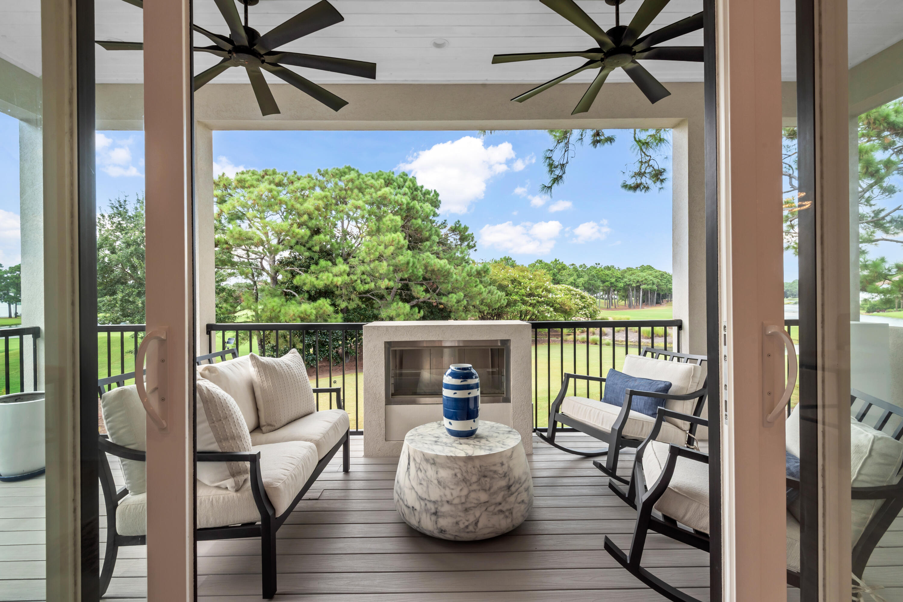 Covered patio with fireplace, cushioned seating, and views across a tree-lined golf course.