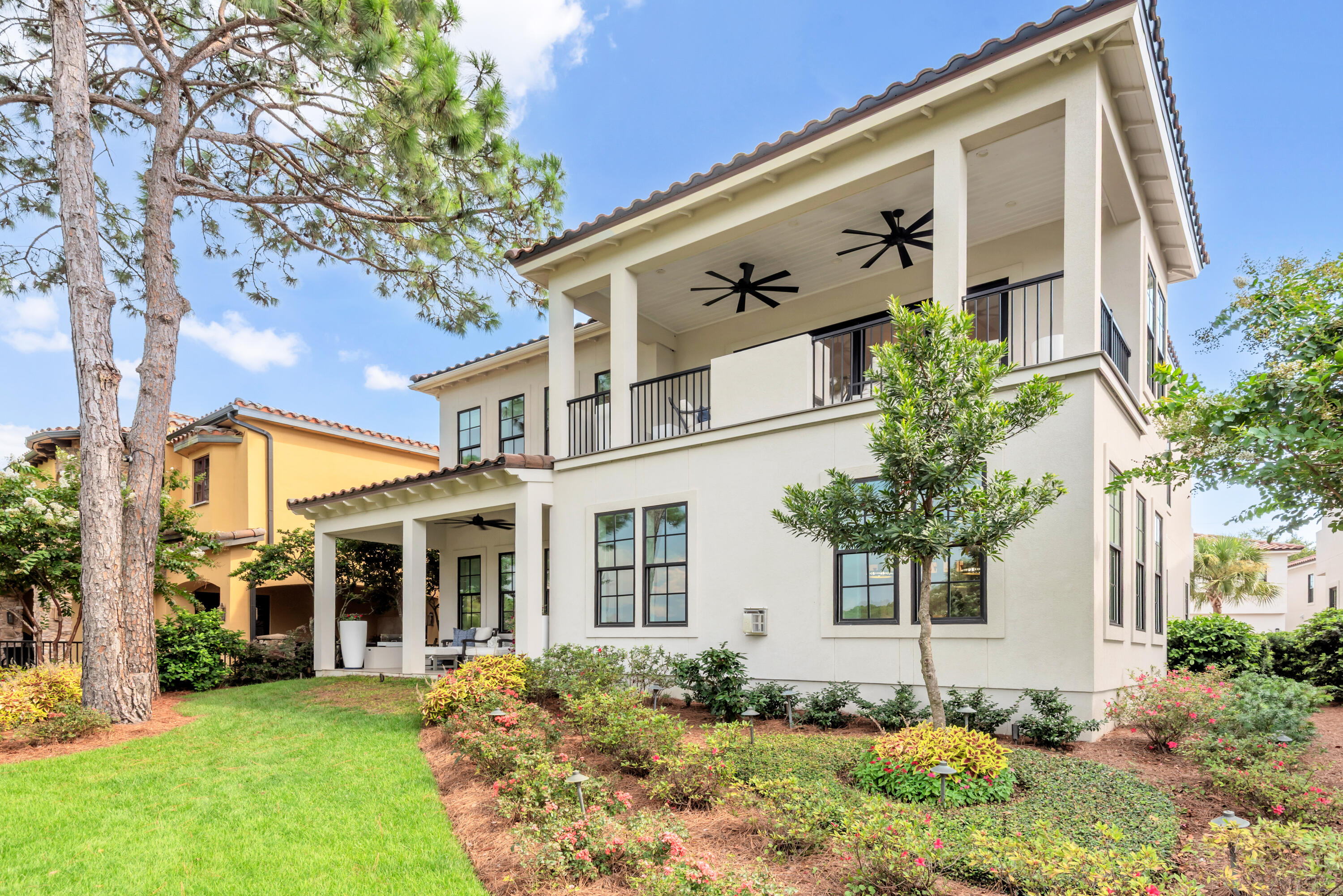 Two-story cream stucco home with covered balconies, ceiling fans, and landscaped grounds.