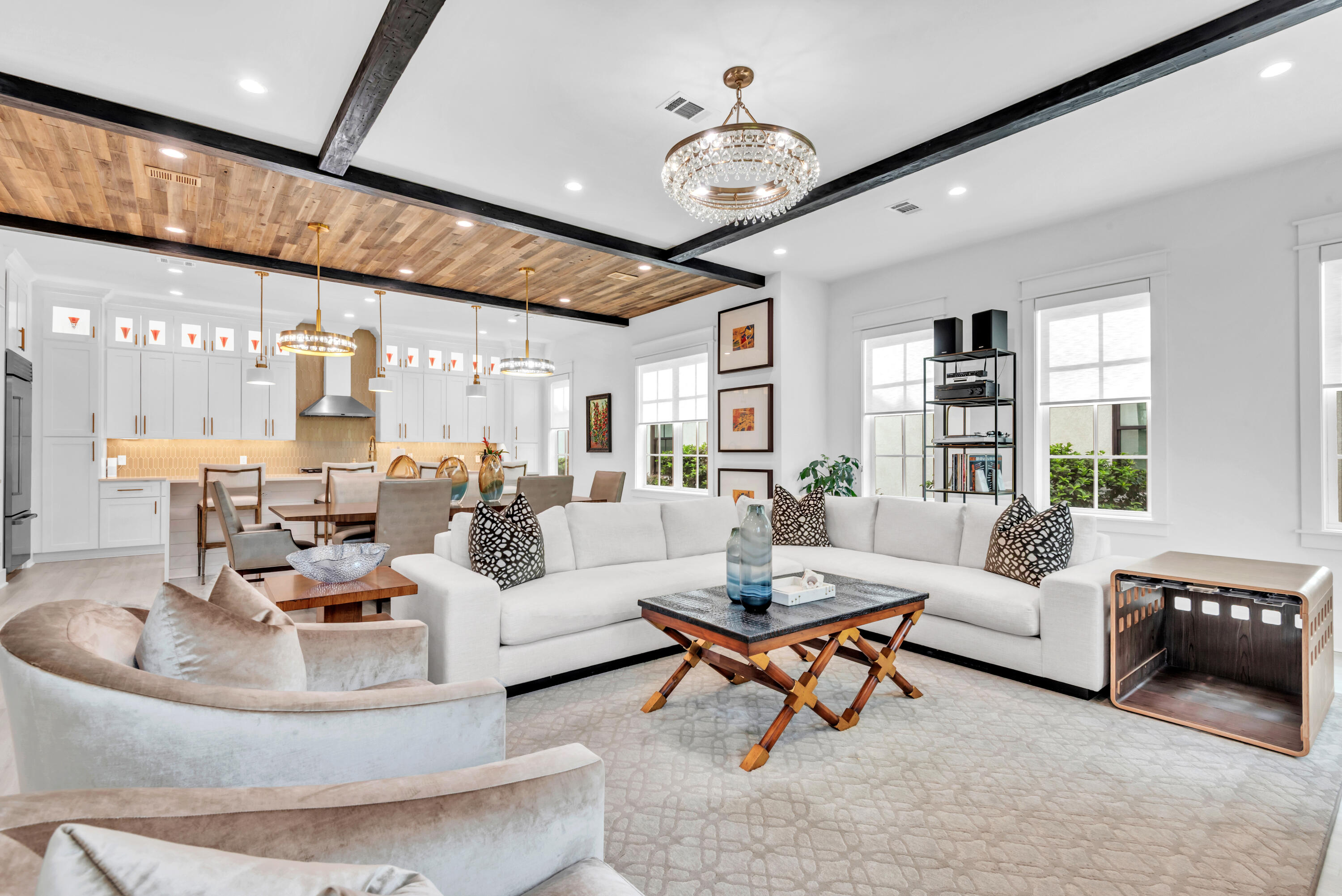Open-plan living room and kitchen with a white sectional, wood-plank ceiling, and dark exposed beams.