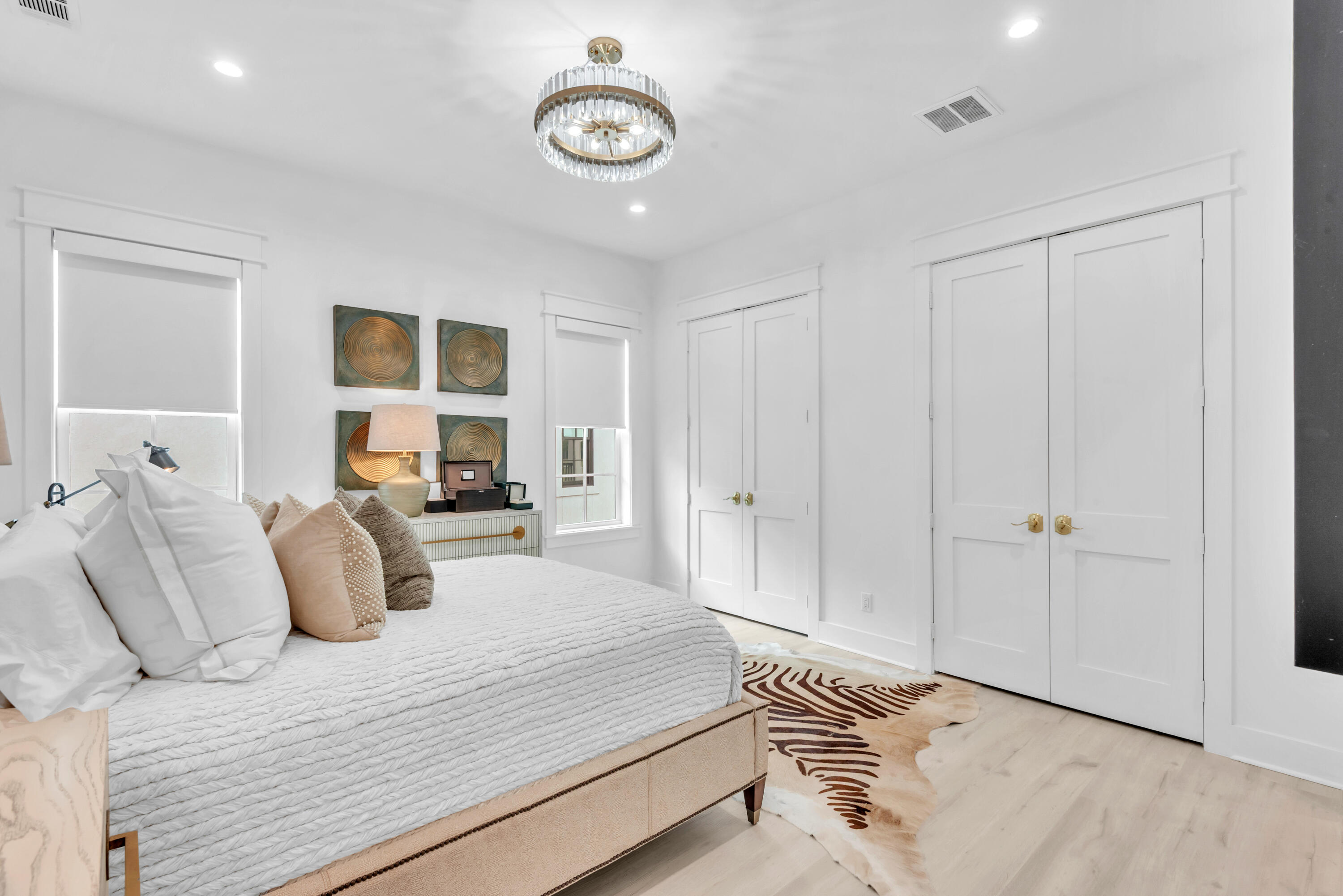 Staged bedroom with a white quilted bed, crystal chandelier, and white double doors.
