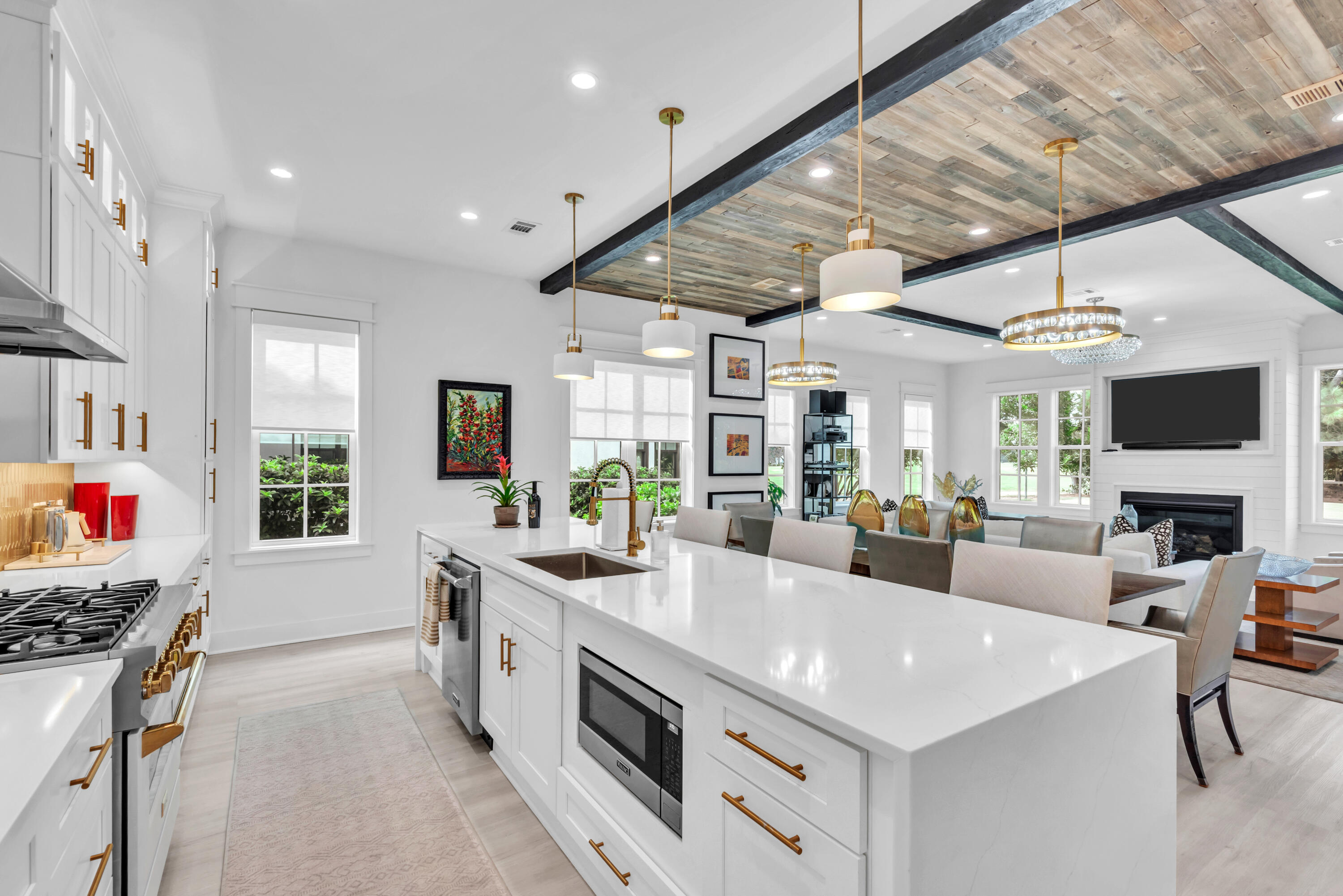 Open-plan kitchen with a large white island, gold fixtures, and a wood-paneled ceiling beside the dining and living areas.