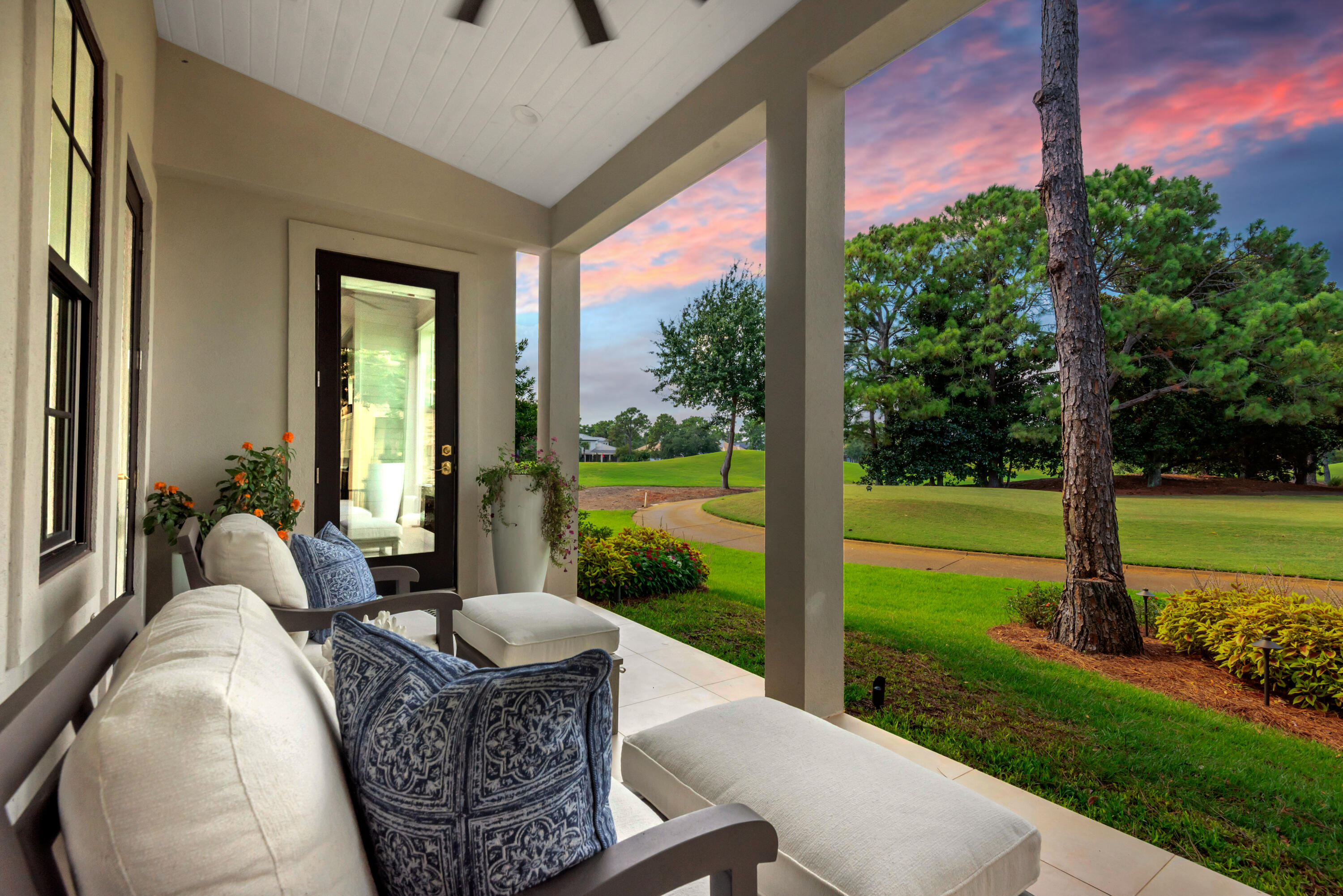 Covered porch with cushioned seating overlooking a golf course beneath a pink dusk sky.