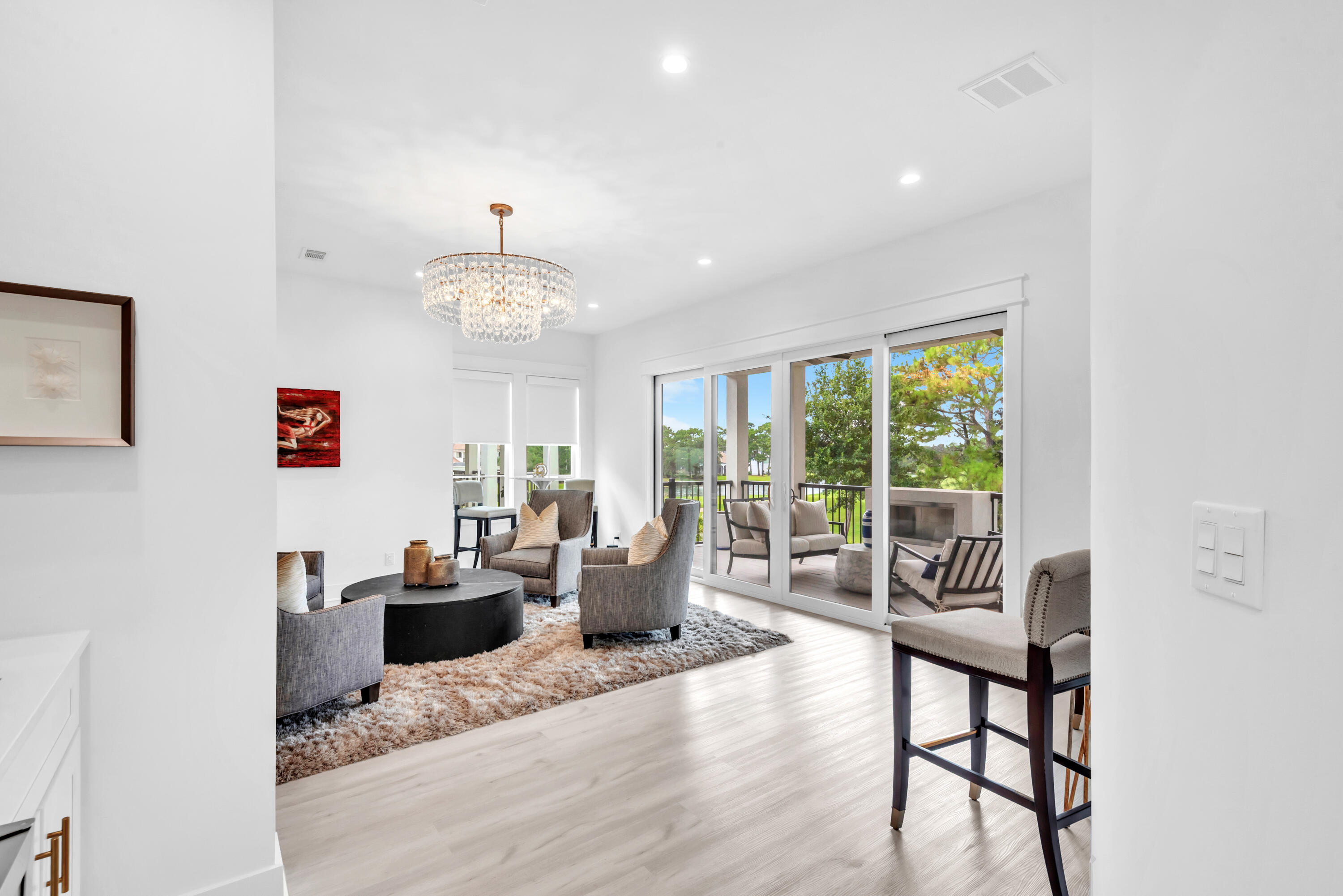 Bright living room with a crystal chandelier and sliding doors opening to a tree-lined patio.