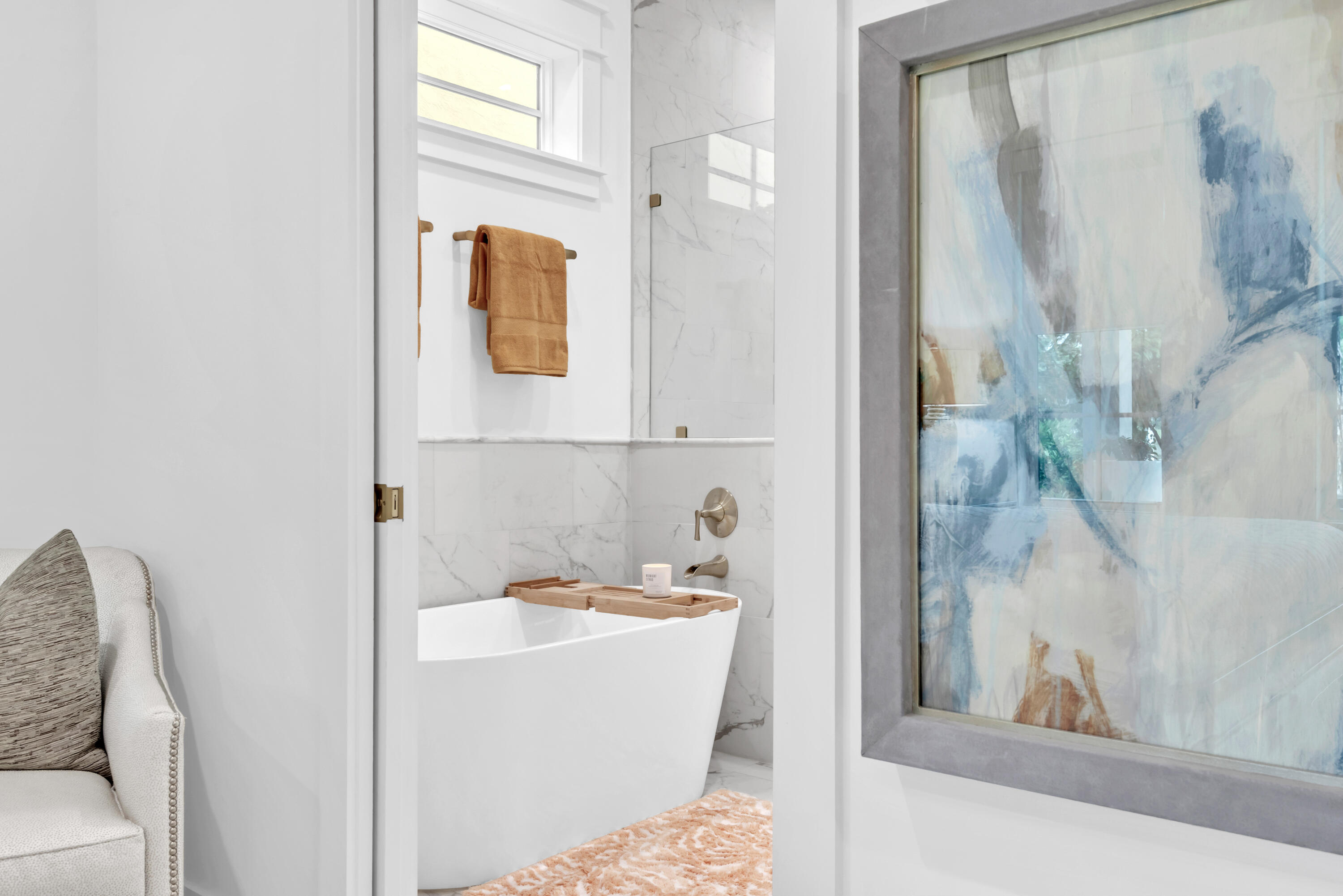 Bathroom with a freestanding tub, marble-look tile, tan towels, and large abstract artwork.