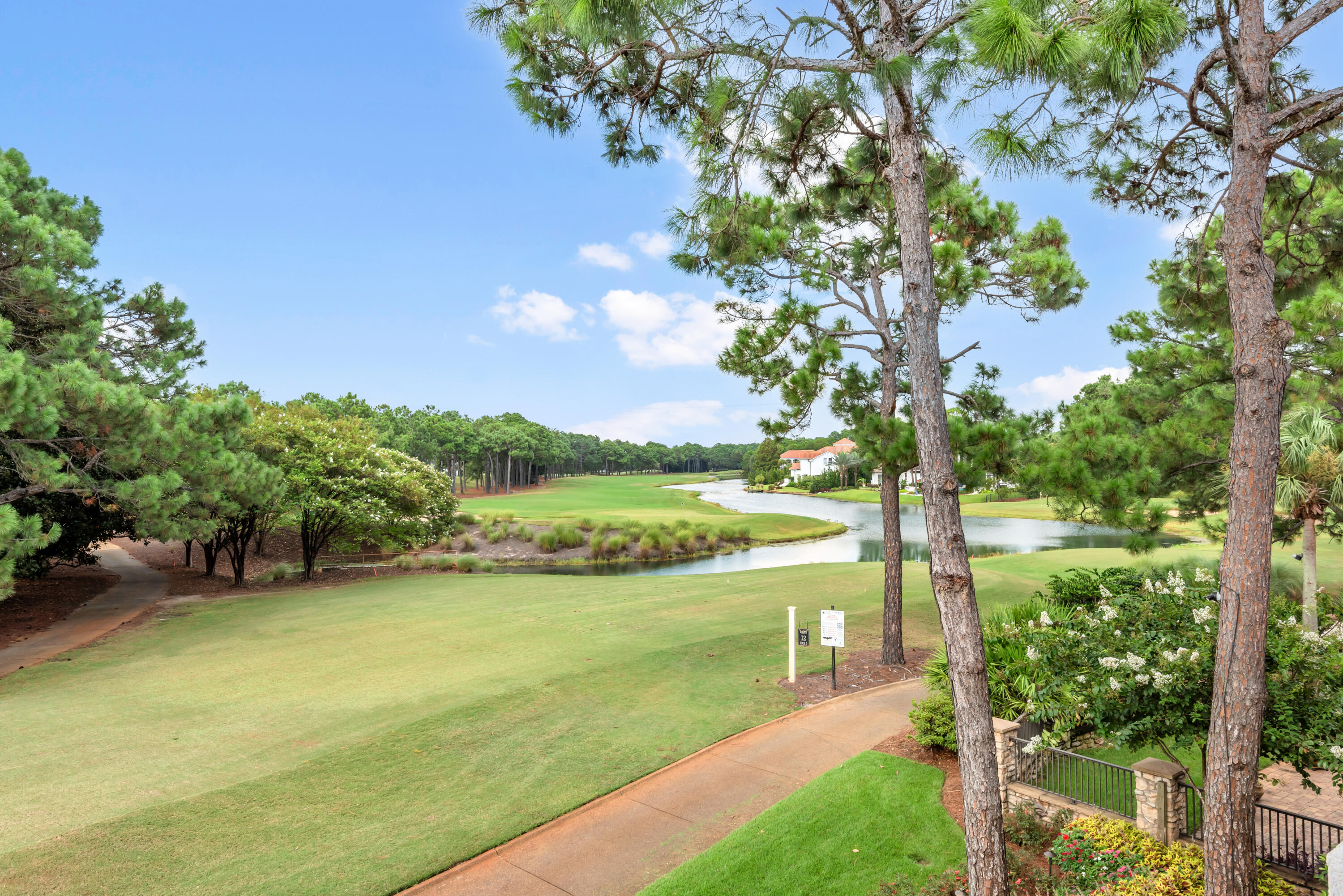Golf course with a winding water hazard, pine trees, and homes beyond the fairway.