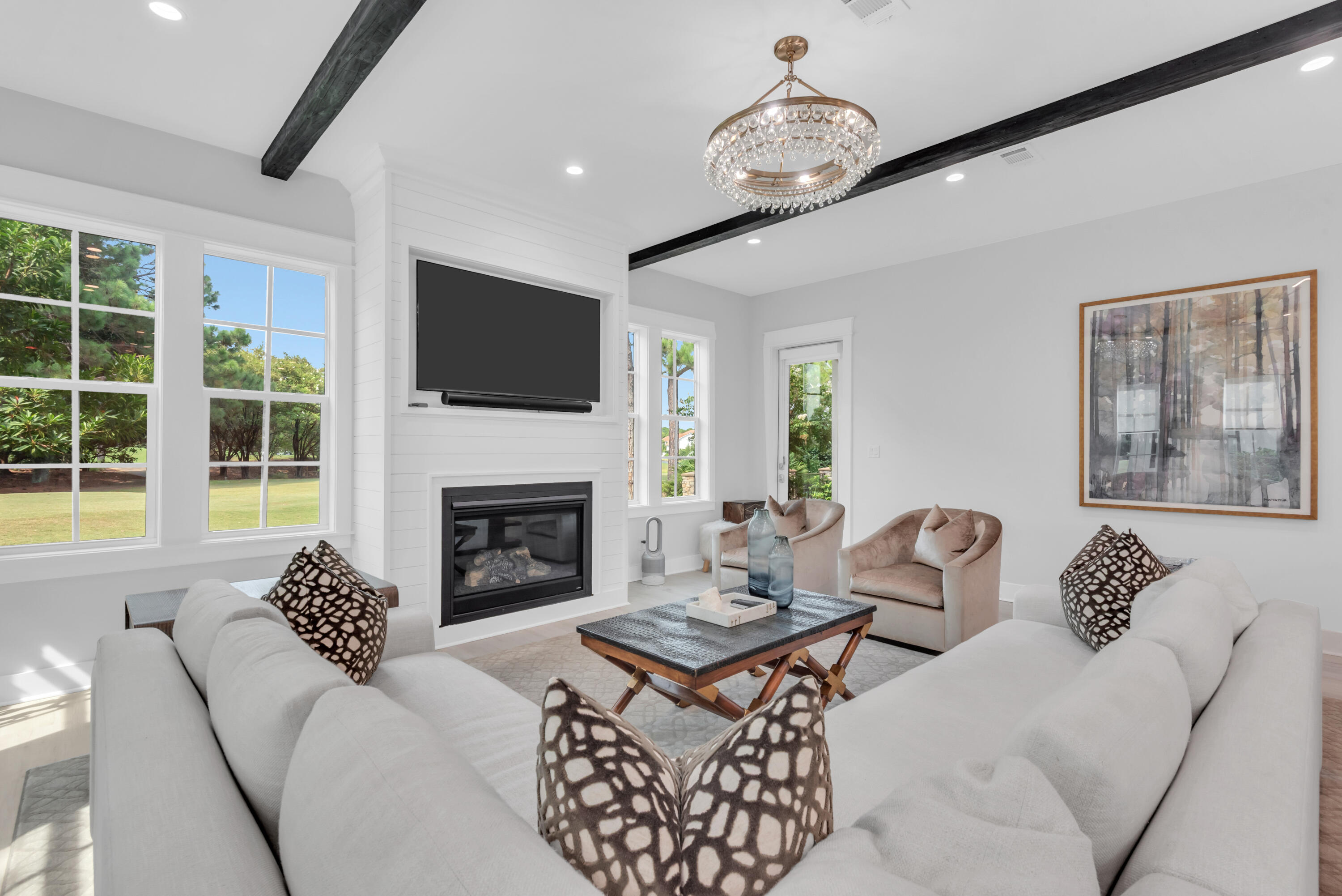Living room with white sofas, a fireplace, large windows, and dark ceiling beams.