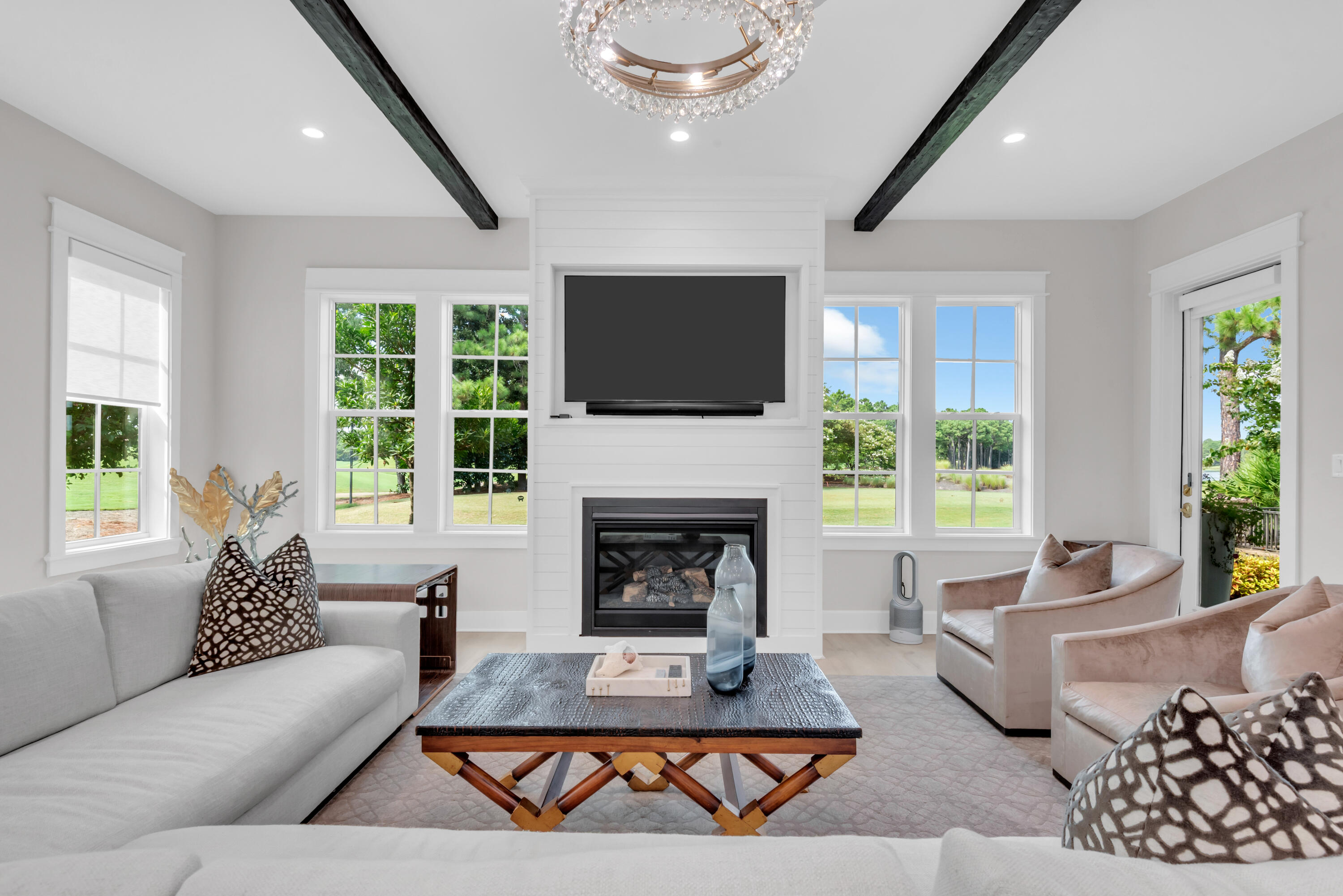 Staged living room with a shiplap fireplace wall, dark ceiling beams, and large windows.