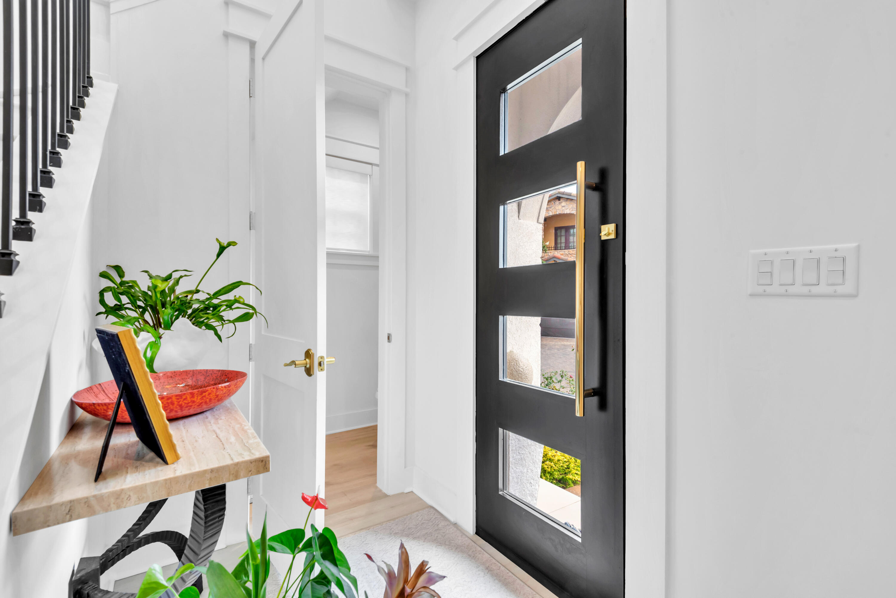 Bright entryway with a black glass-panel front door, brass handle, and stone console table with a red bowl.