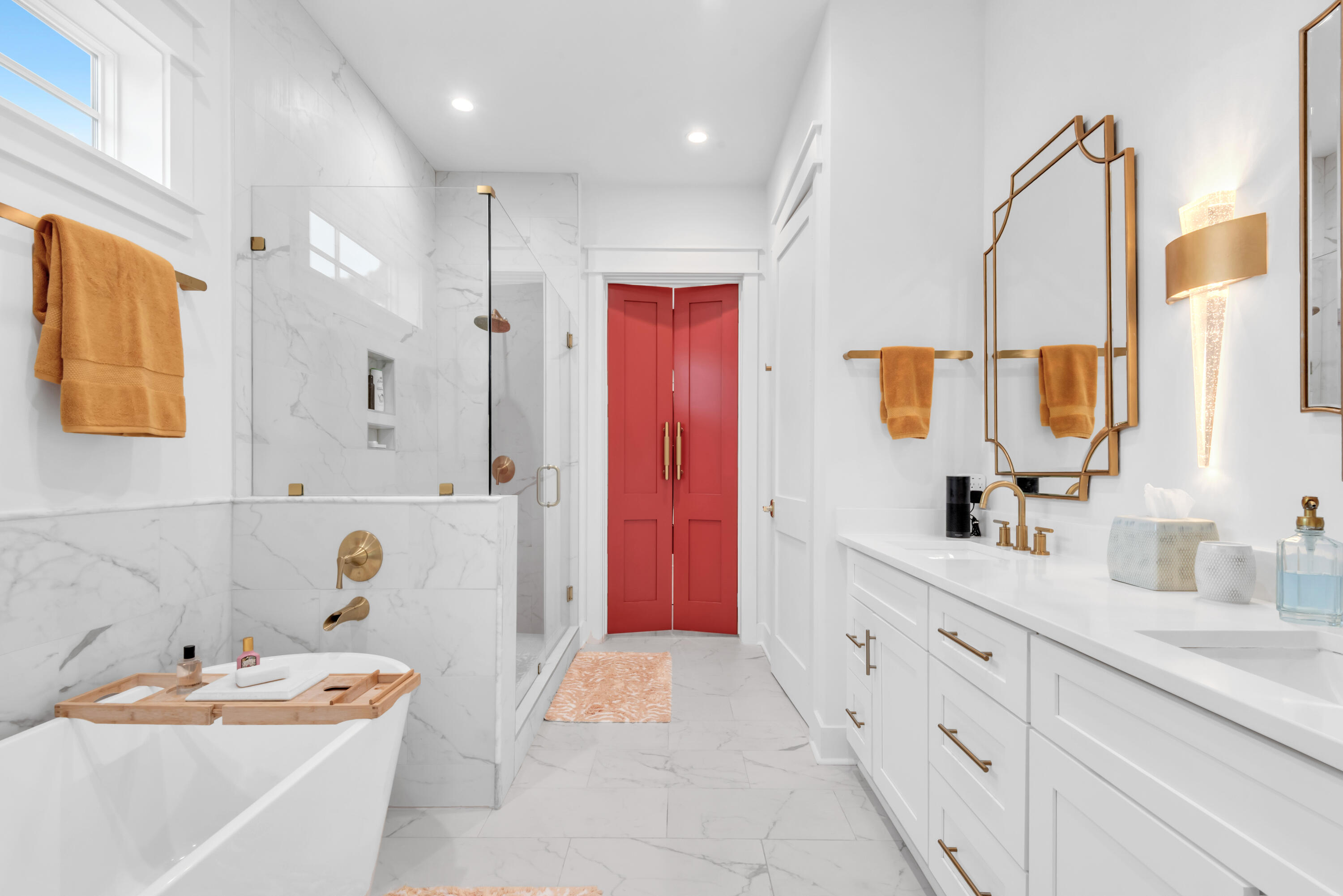 Marble bathroom with a freestanding tub, gold fixtures, and red double doors.