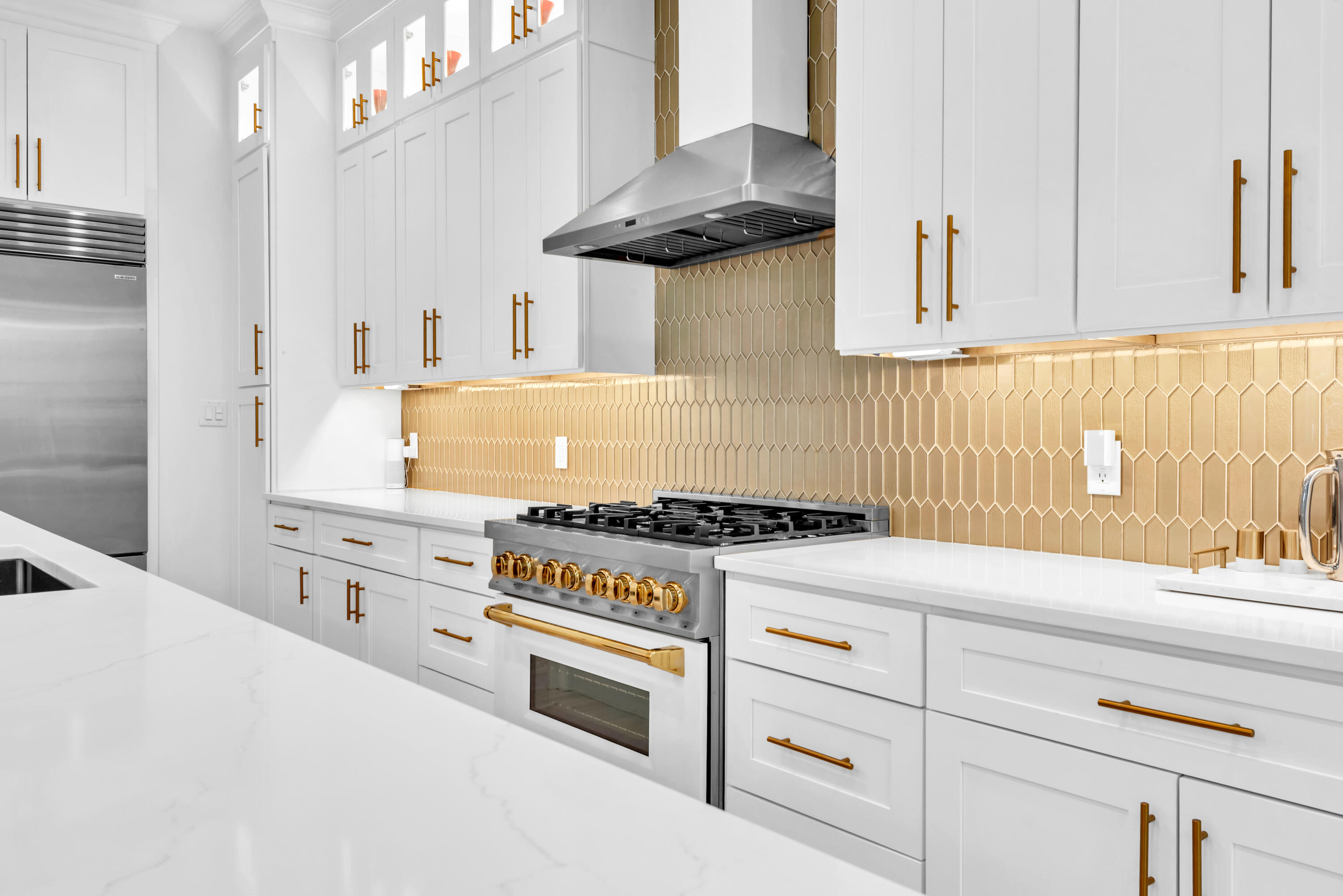 Bright kitchen with white cabinets, brass hardware, a stainless gas range, and gold-toned tile backsplash.