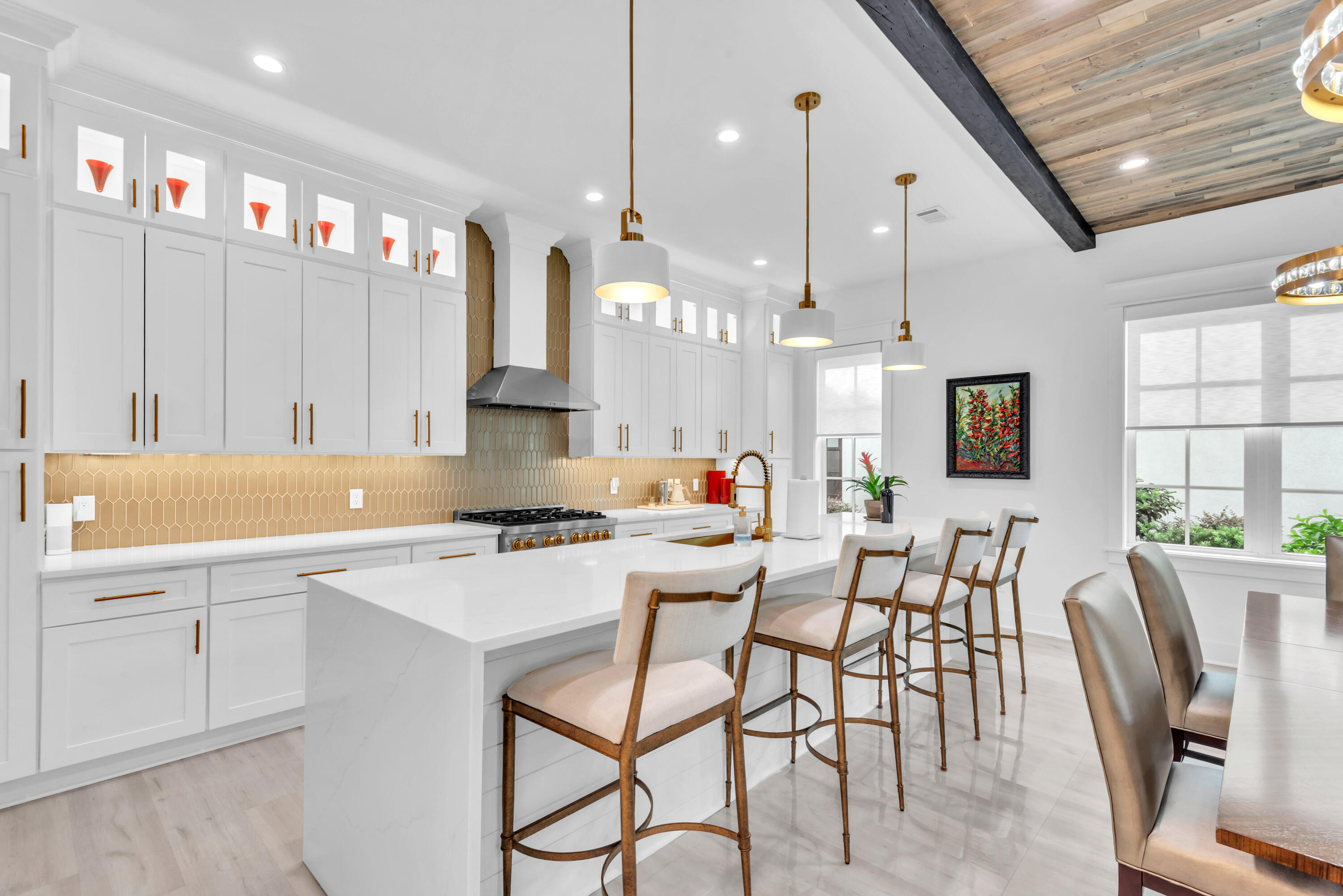 Bright white kitchen with a large island, gold tile backsplash, brass accents, and wood-plank ceiling.