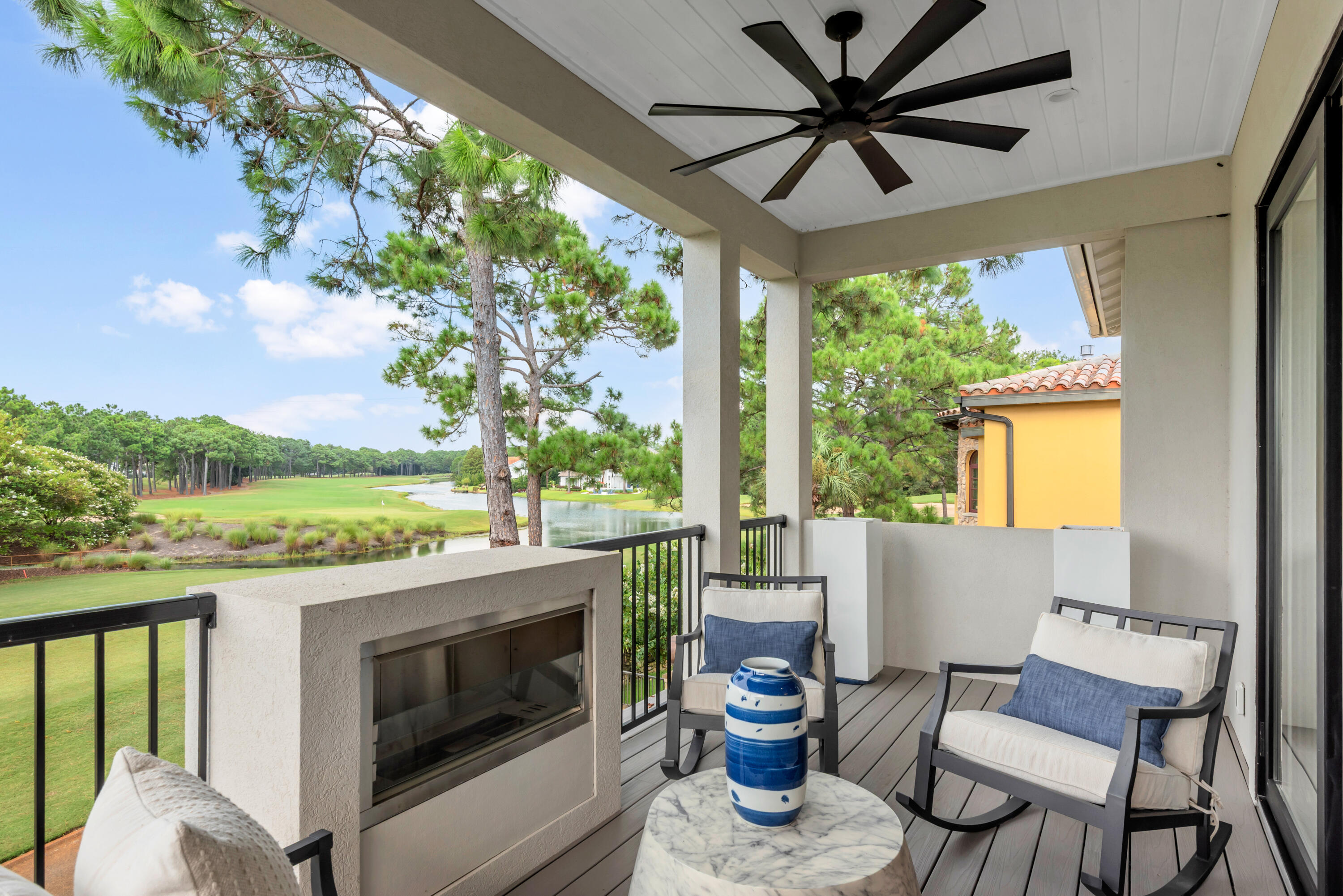 Covered balcony with fireplace and rocking chairs overlooking a golf course and water.