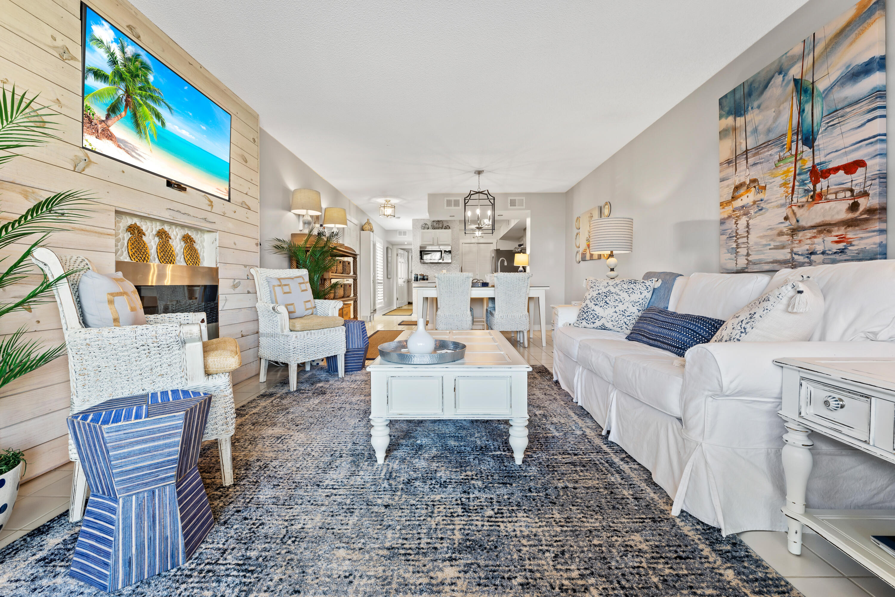 Furnished living room with a white sofa, woven chairs, fireplace, and open dining area.