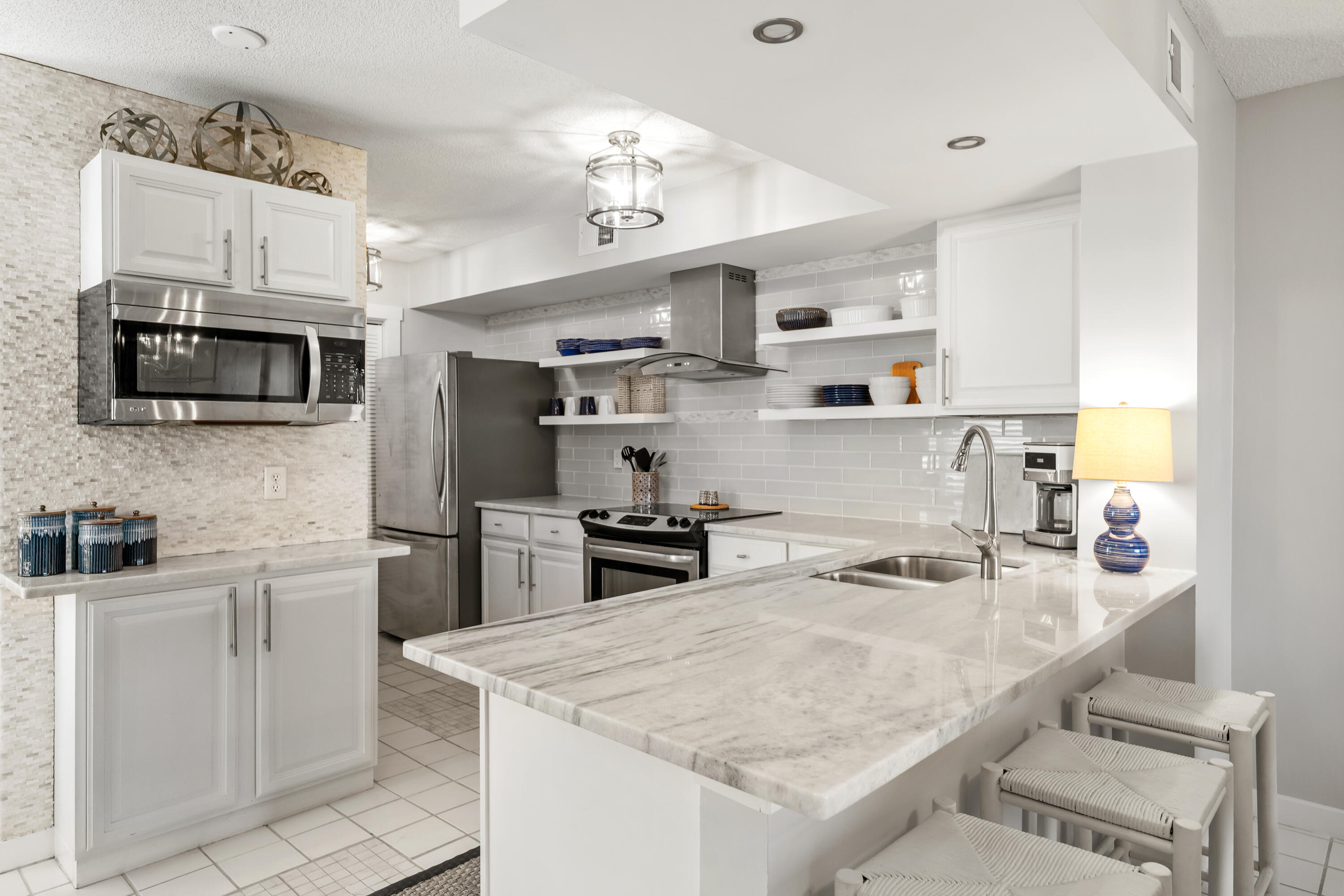 Renovated kitchen with stainless steel appliances and a marble-look island with sink and bar stools.