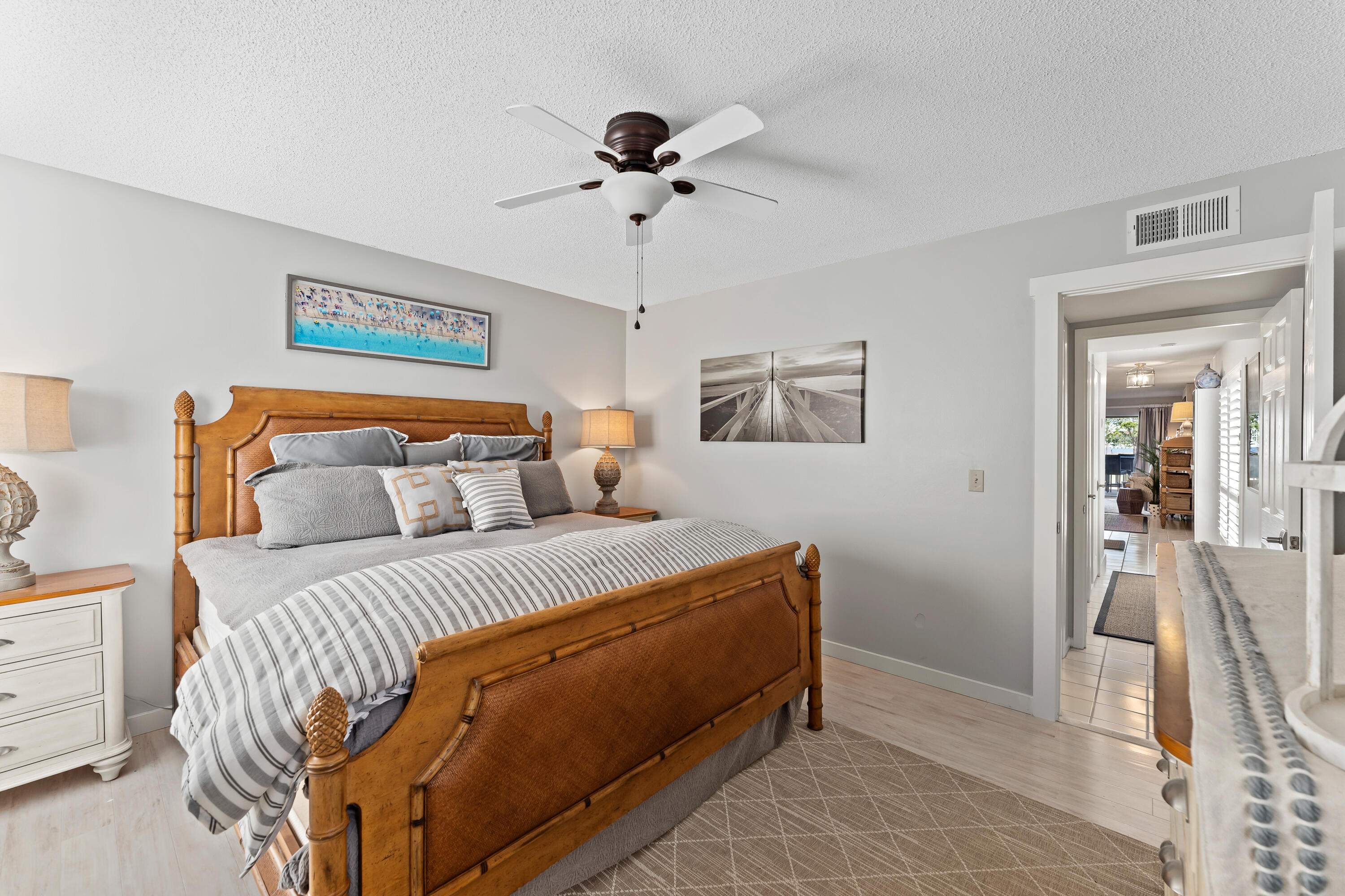 Bedroom with a carved wooden bed, striped gray bedding, and a view through the doorway to the living area.