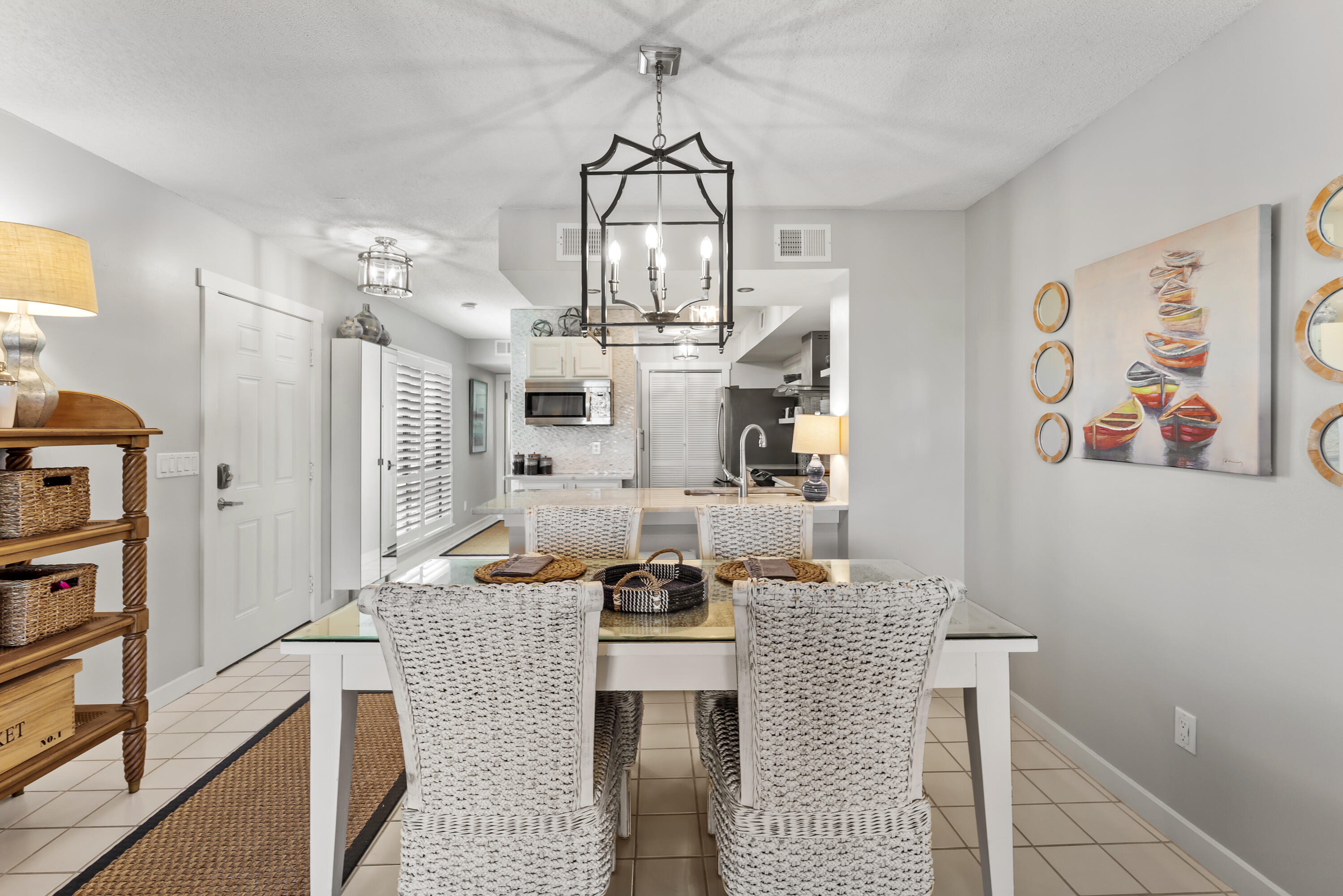 Dining room with woven chairs and a glass-top table opening into a bright kitchen.